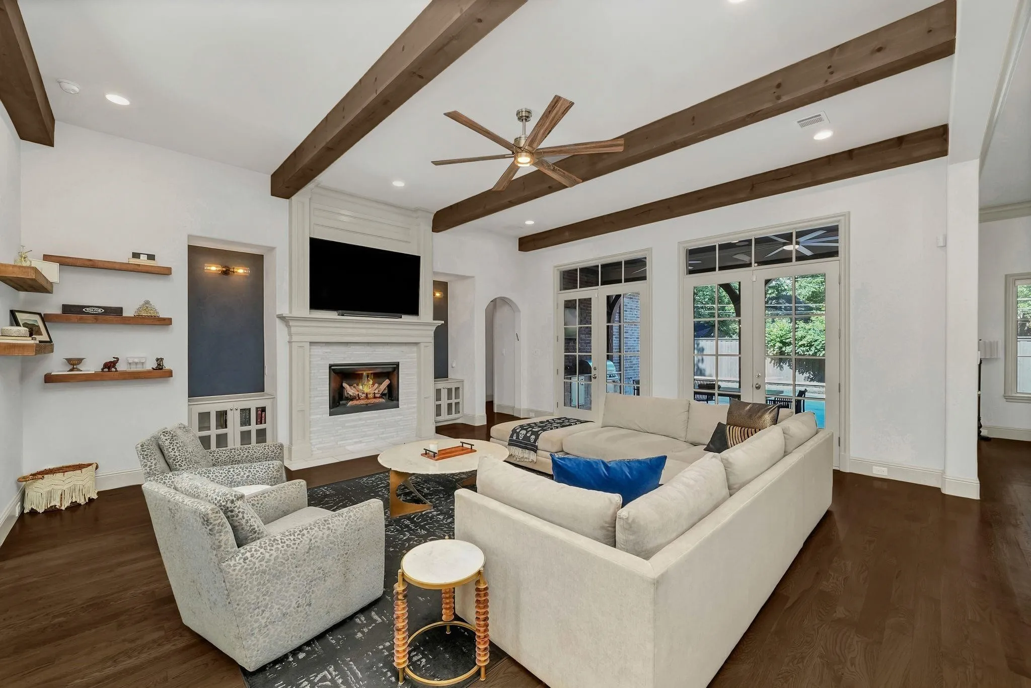 Spacious living area featuring exposed wood ceiling beams, a white brick fireplace with a detailed mantel, and dark wood-finish flooring