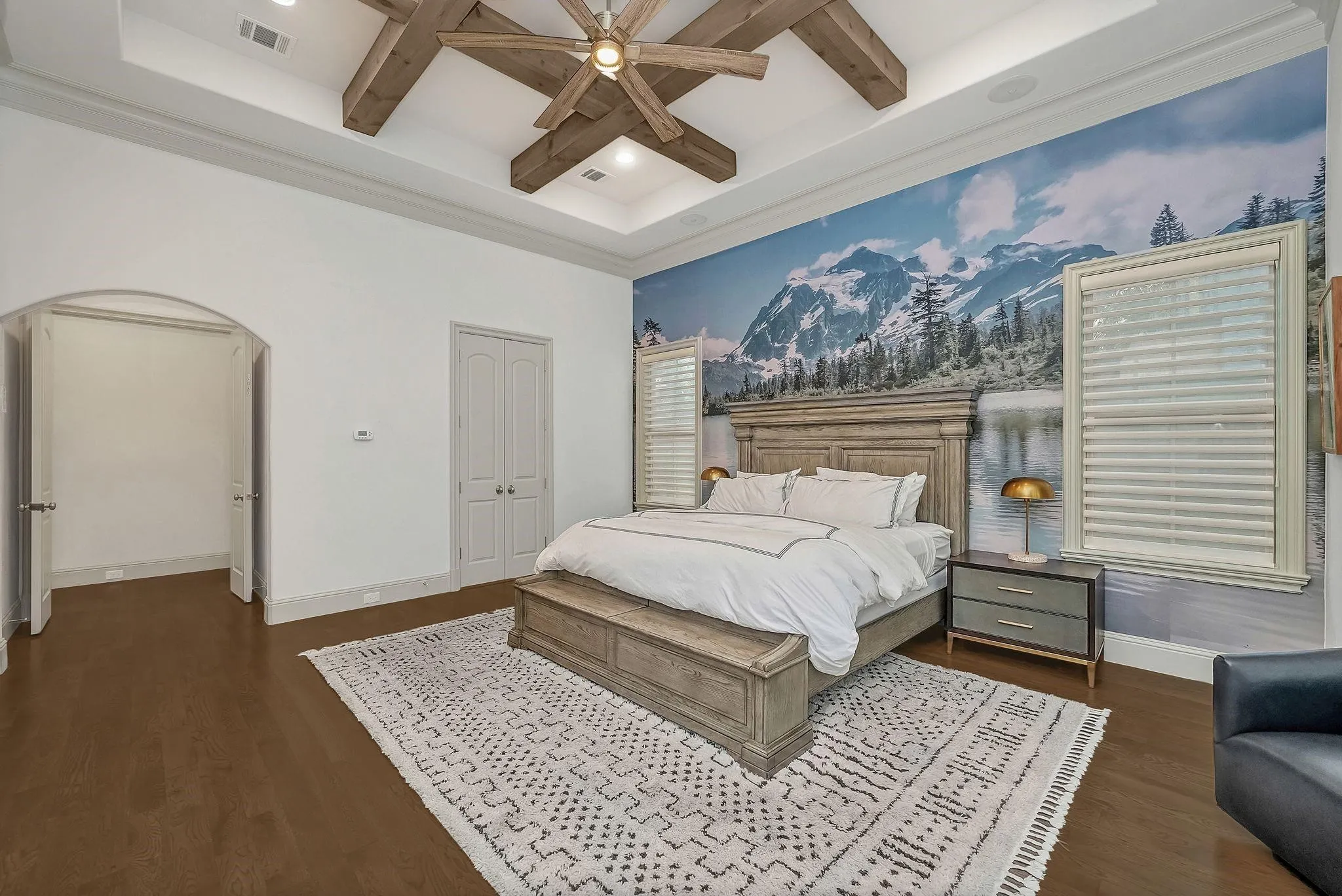 Bedroom with wood-finish flooring, tray ceiling with exposed wood beams, and a ceiling fan