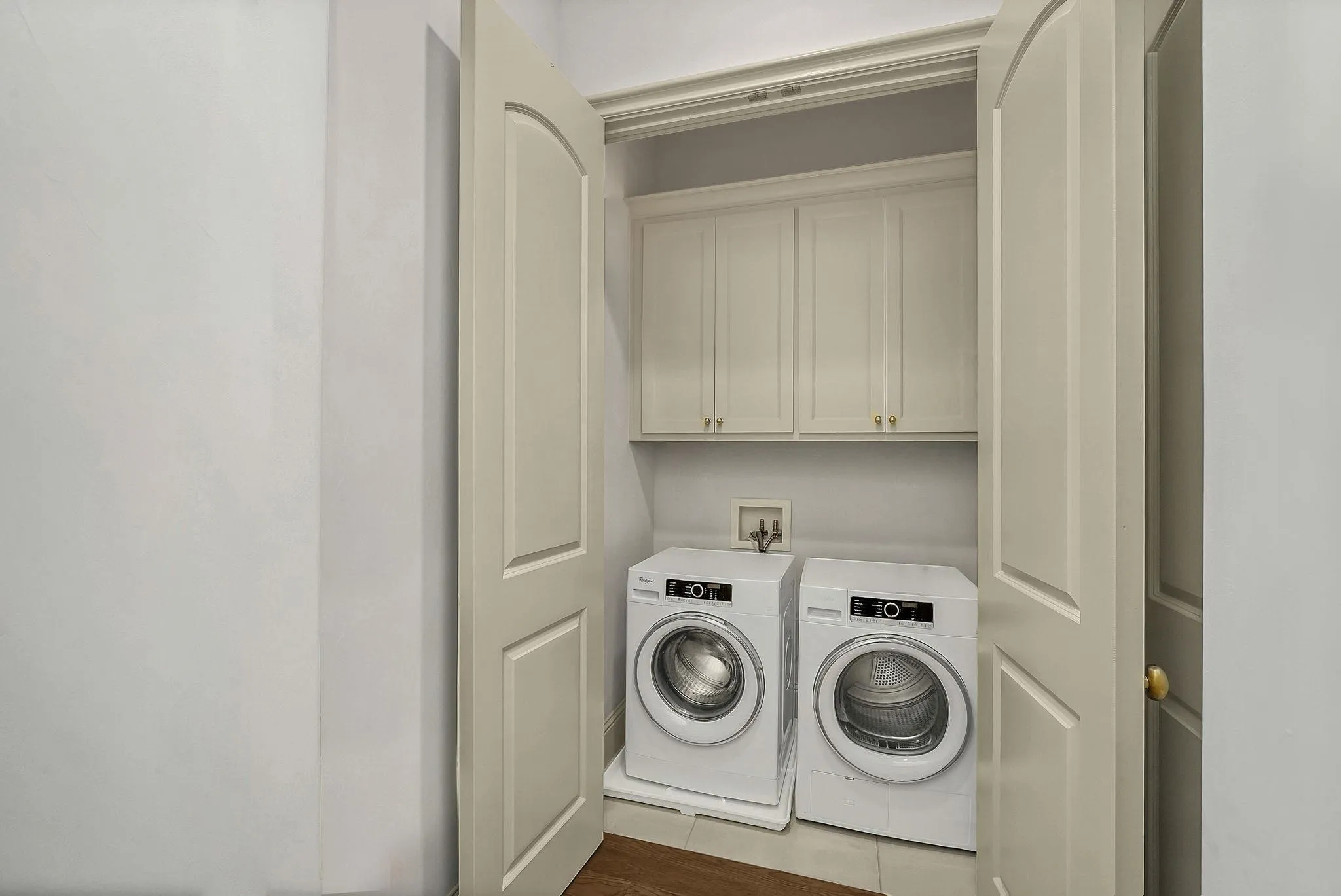 Dedicated laundry closet featuring double doors, upper cabinetry, and tile flooring