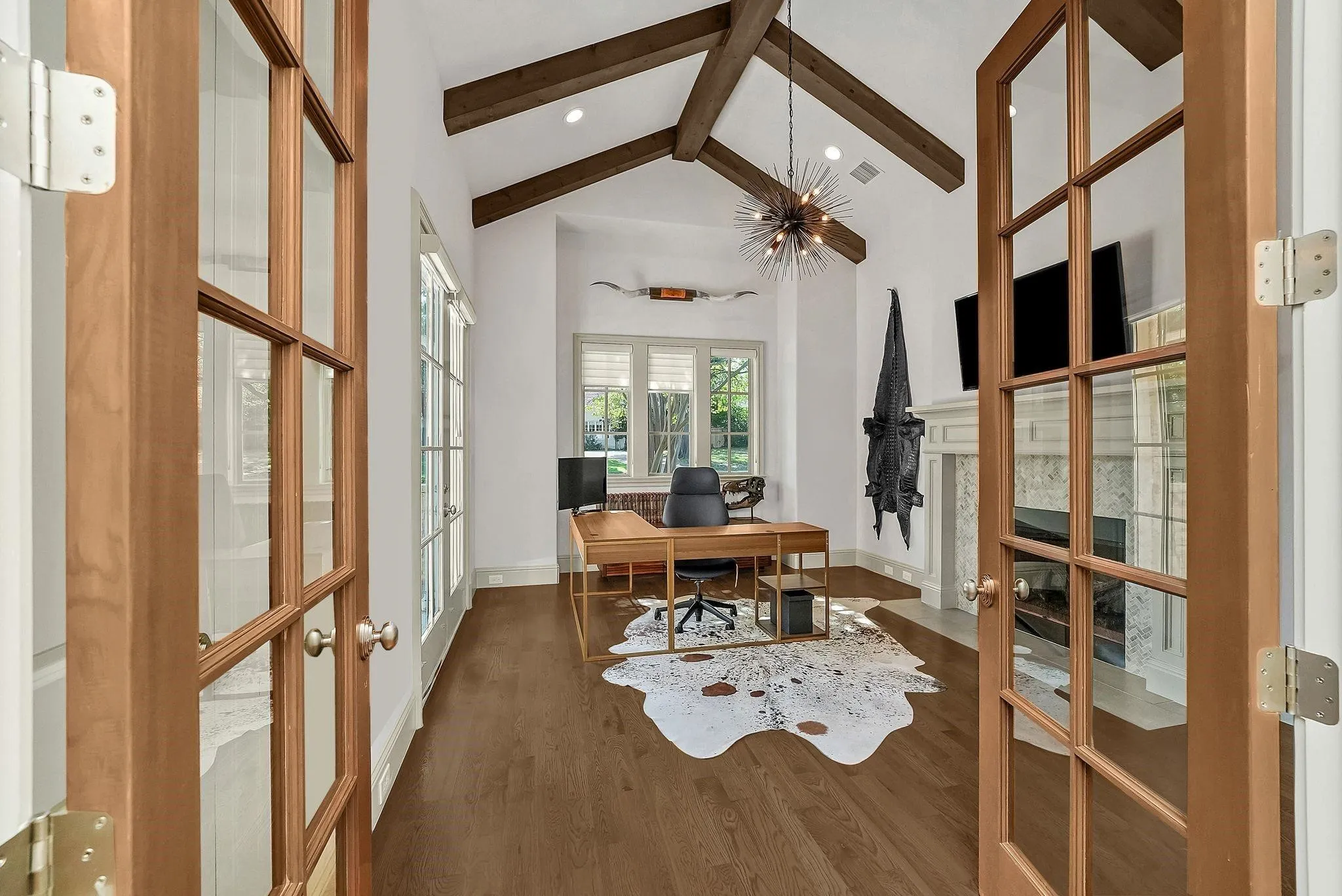 Vaulted ceiling with exposed wood beams, wood-finish flooring, and a stone fireplace with a white mantel