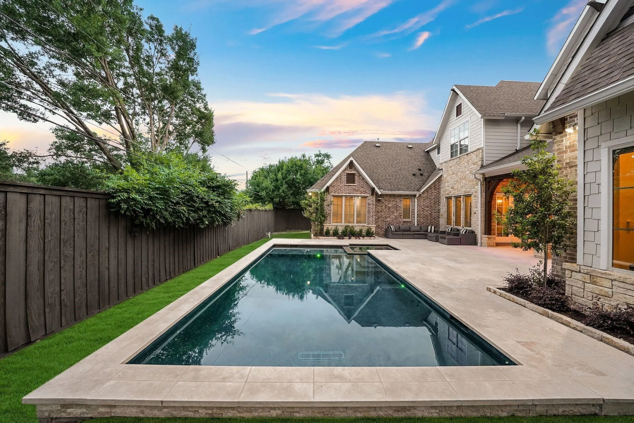 Expansive backyard featuring a rectangular swimming pool with stone coping, surrounding paved patio, manicured lawn, and a tall privacy fence