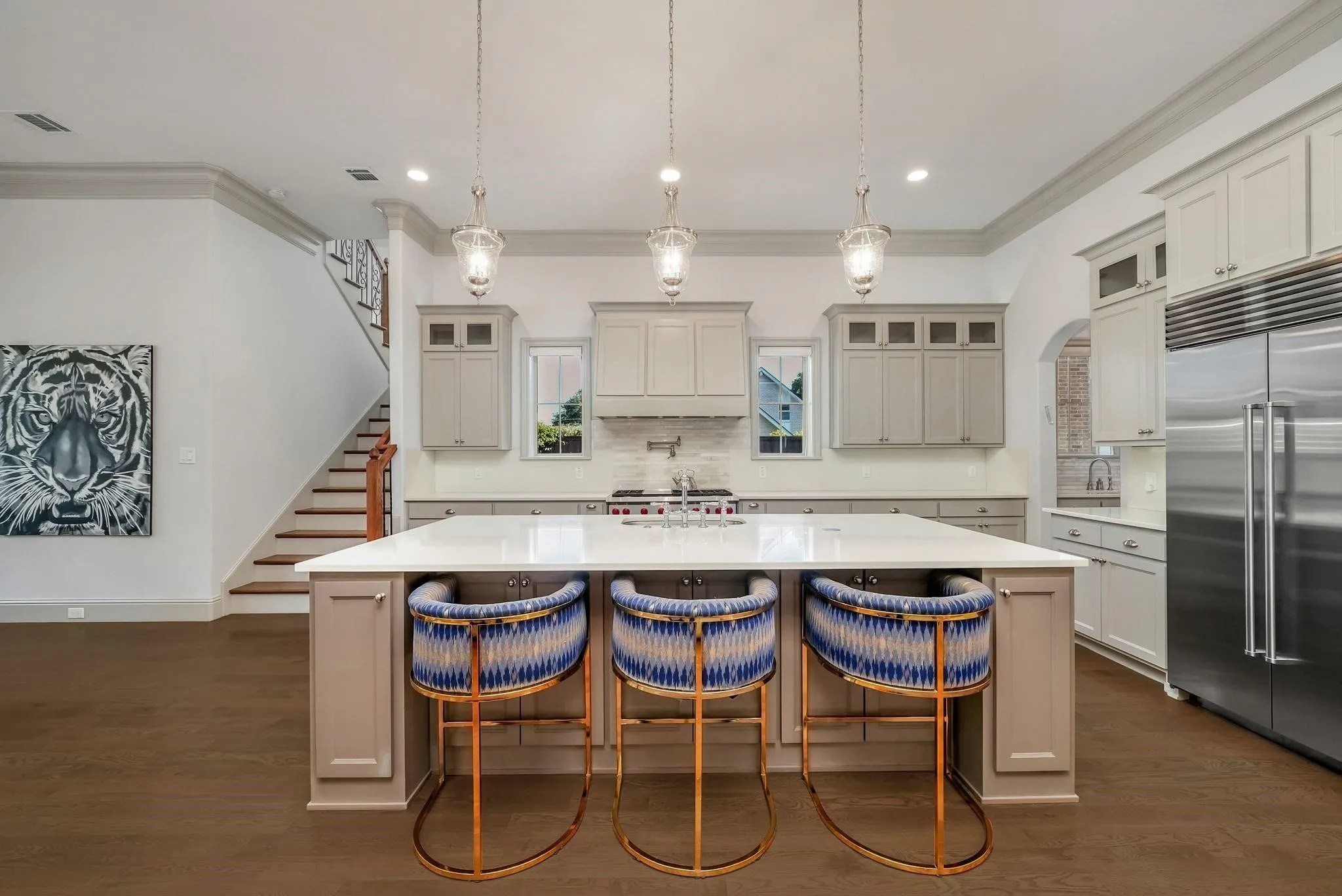 Contemporary kitchen featuring an oversized island with seating, pendant lighting, stainless steel appliances, white cabinetry, and wood-finish flooring