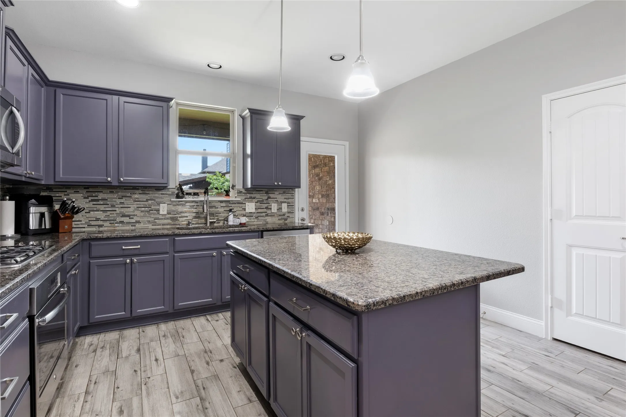 Kitchen featuring a central island with a stone-finish countertop, wood-finish flooring, recessed lighting, pendant lighting, and gray cabinetry with stainless steel hardware