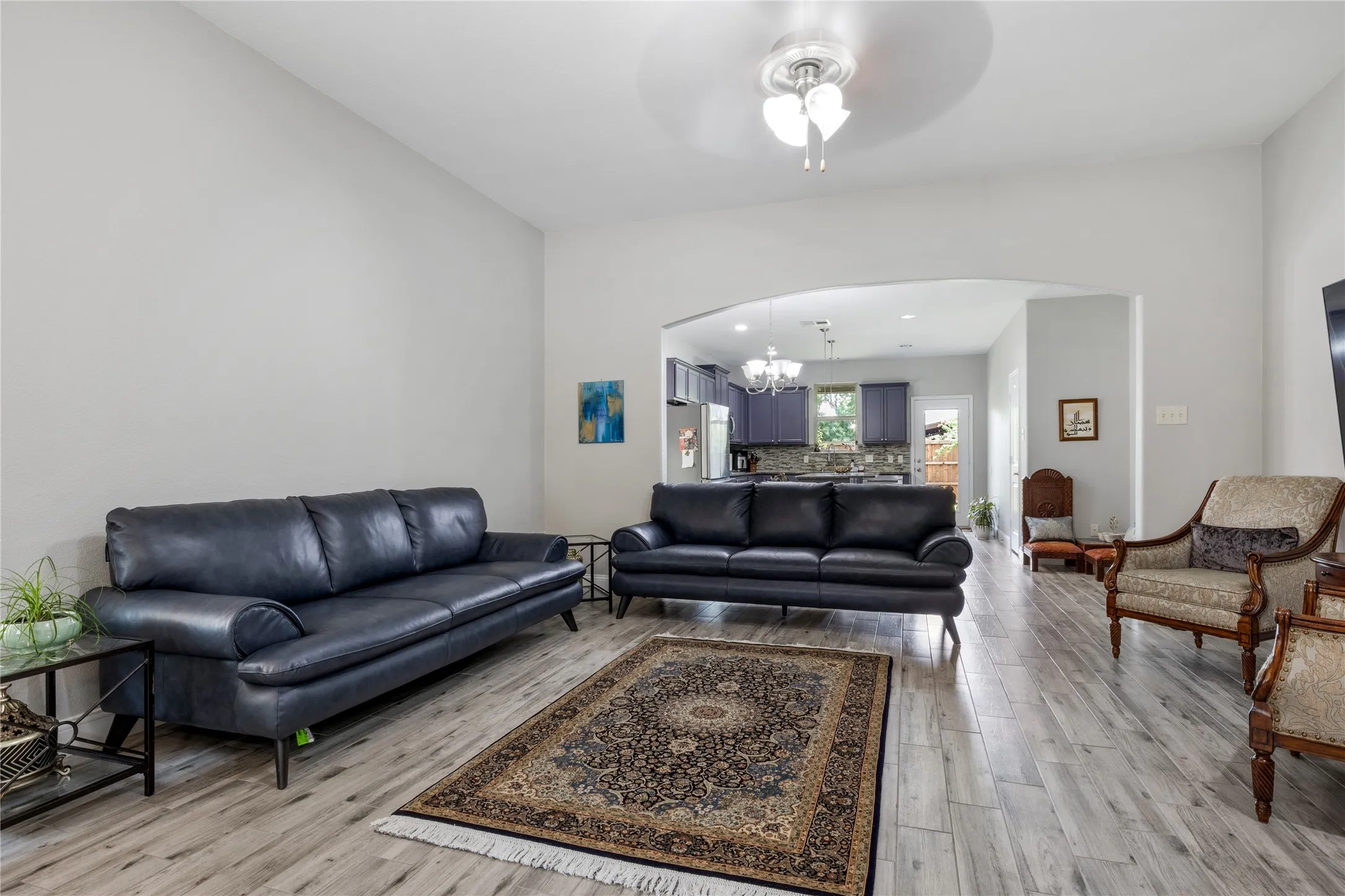 Spacious living area featuring light wood-finish flooring, vaulted ceilings, and a ceiling fan with integrated lighting