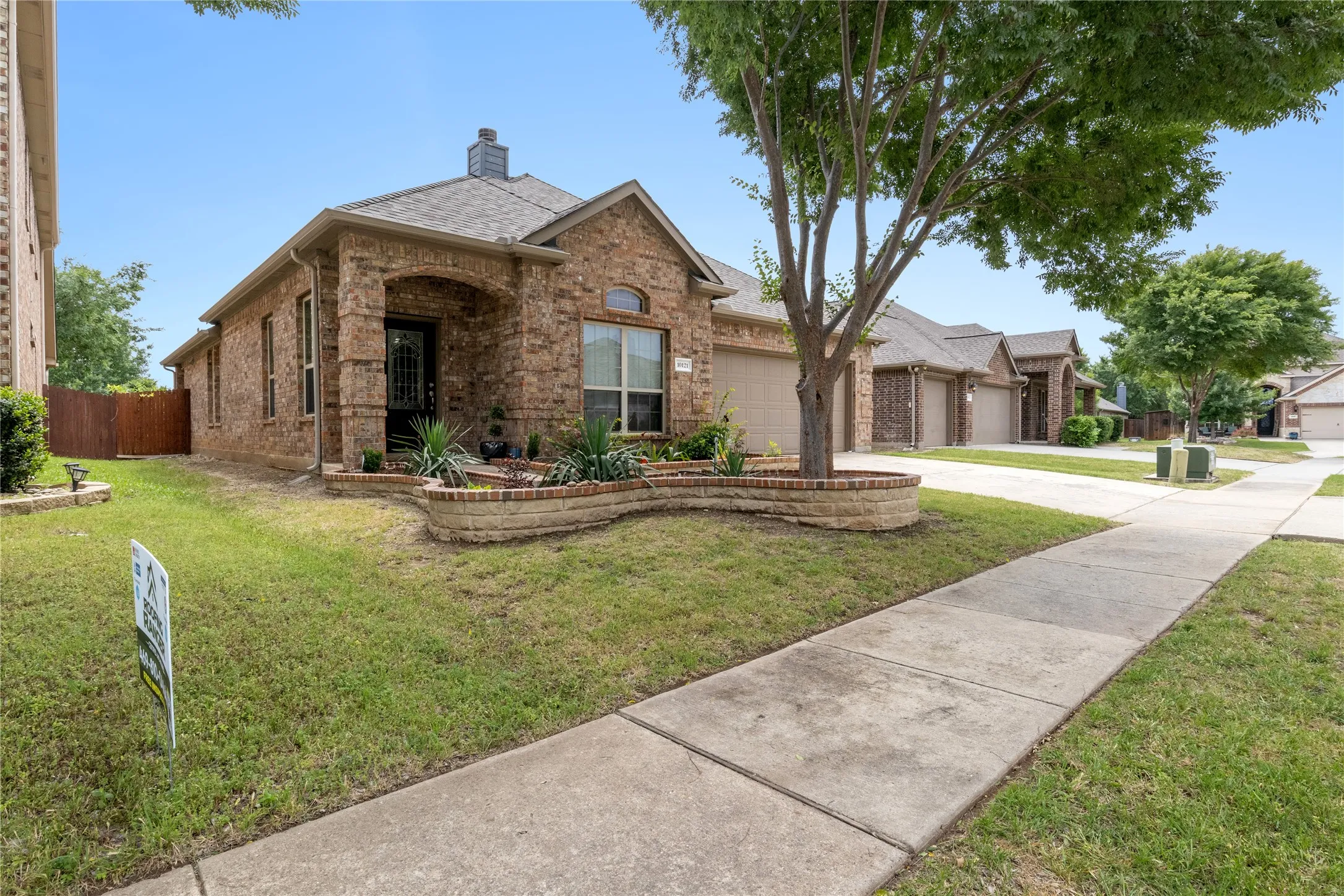 Brick exterior with arched entryway, a landscaped front bed, and a mature tree