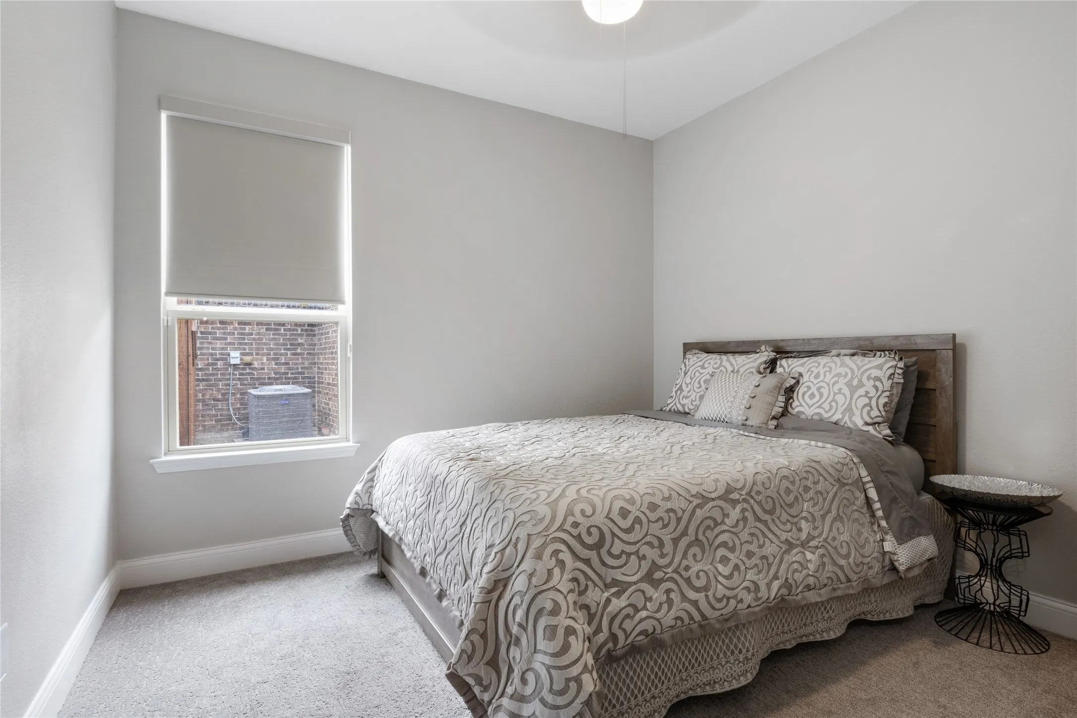 Carpeted room with light grey walls, a single window featuring a roller shade, and a wood-finish headboard