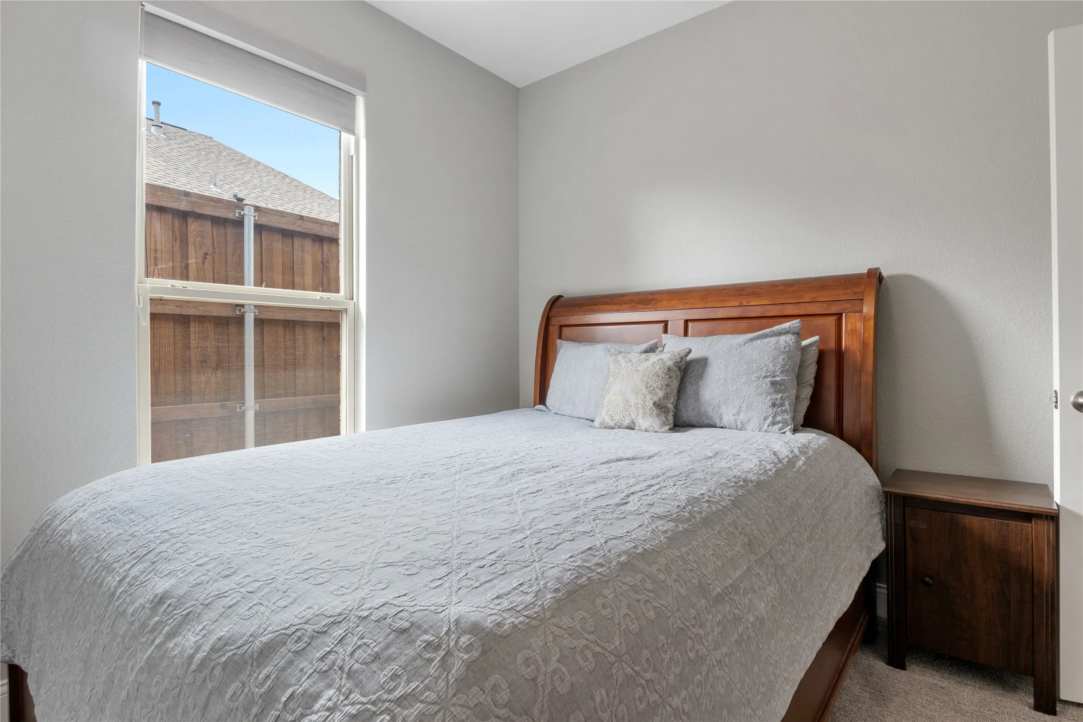 Carpeted room with light gray walls and a single window featuring a roller shade