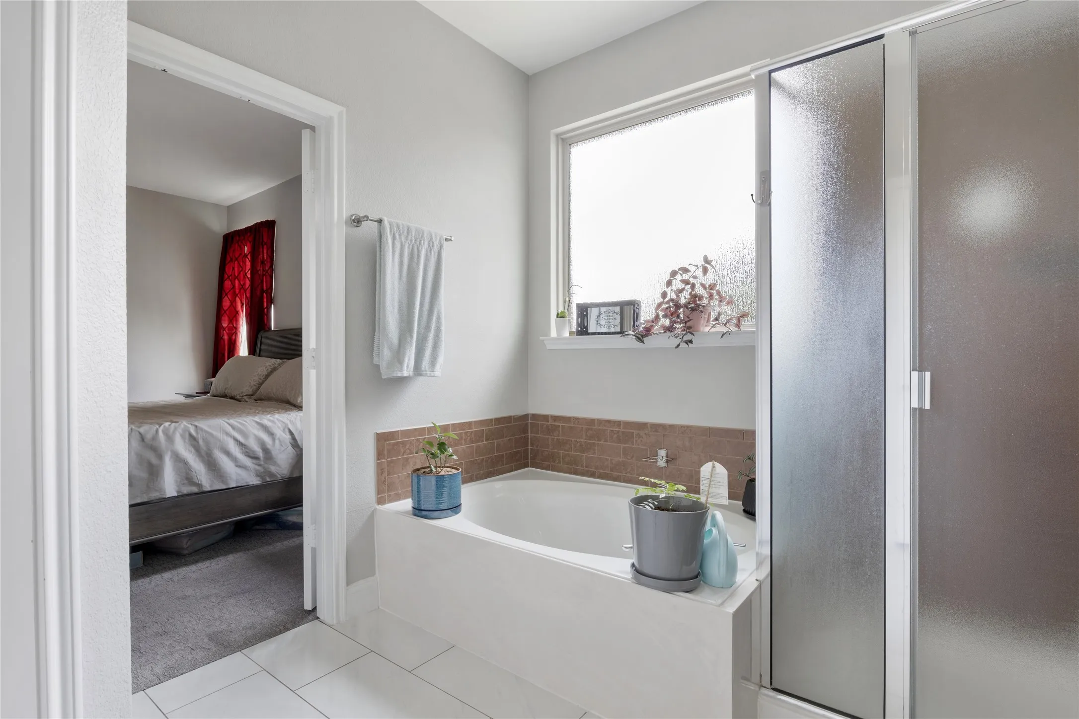 Soaking tub with a tiled surround, frosted glass shower enclosure, and white tile flooring
