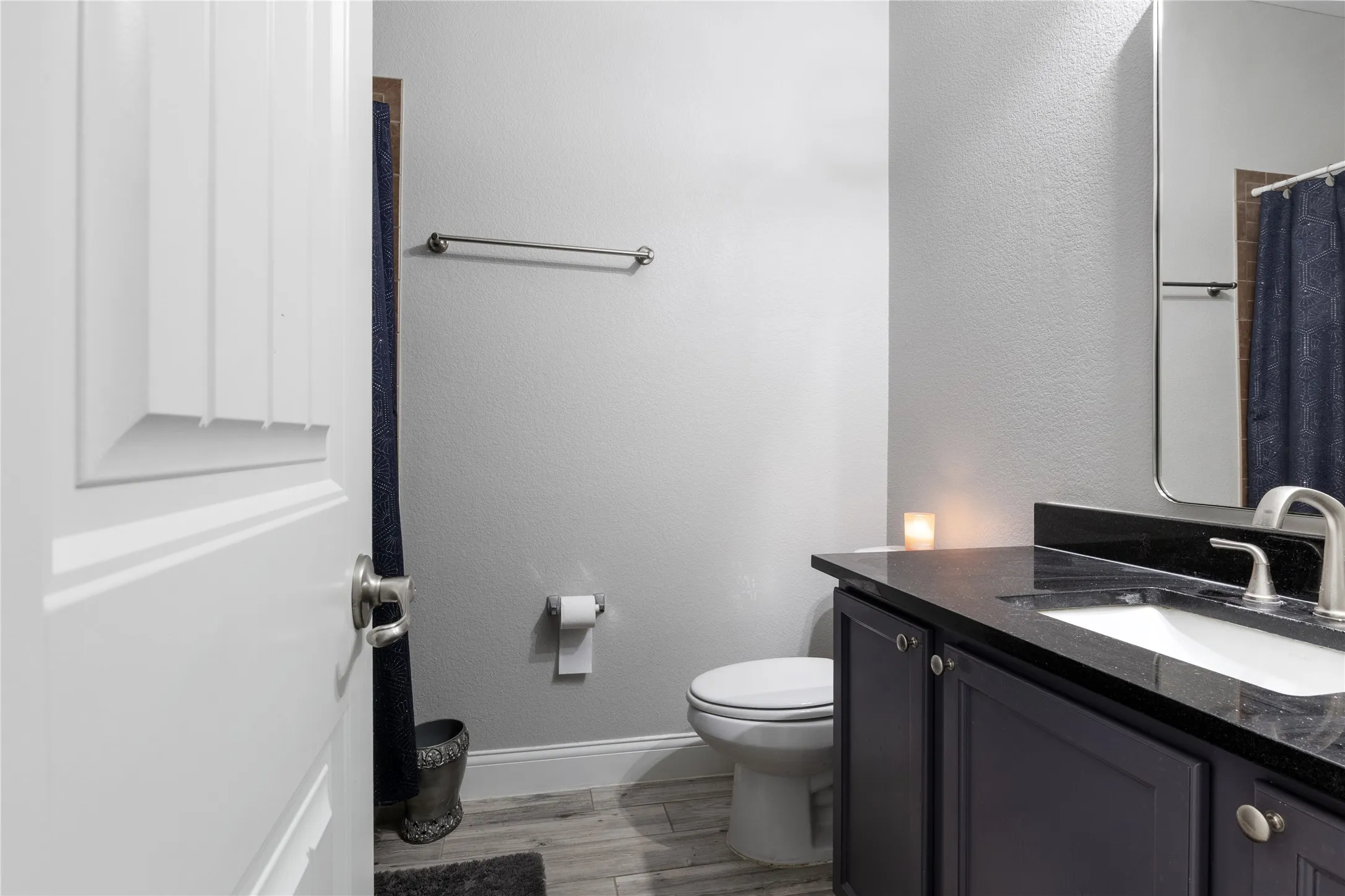 Bathroom featuring wood-finish flooring, a toilet, a vanity with a dark countertop and undermount sink, and a framed mirror