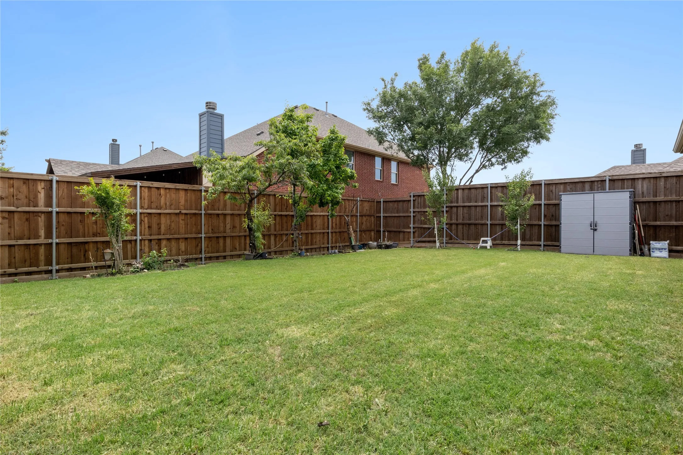 Expansive backyard featuring a manicured lawn, full wood privacy fencing, and mature trees
