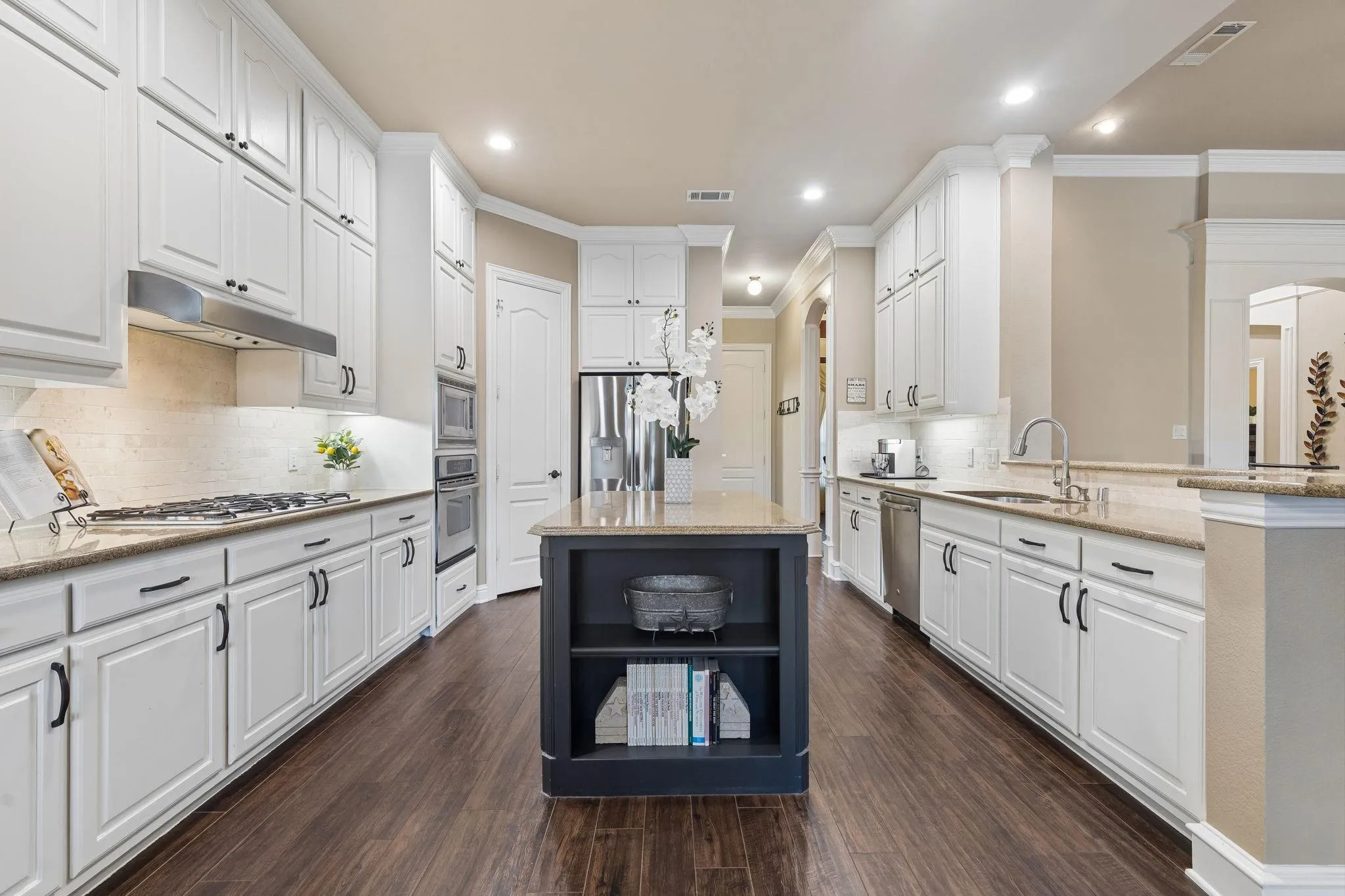 Welcome to the HUGE kitchen! Here you will find stainless steel appliances, walk-in pantry, crown molding, new backsplash, under cabinet lighting, wood like tile floors, recessed lighting, granite countertops, soft close cabinets,  and a massive island anchoring the kitchen.