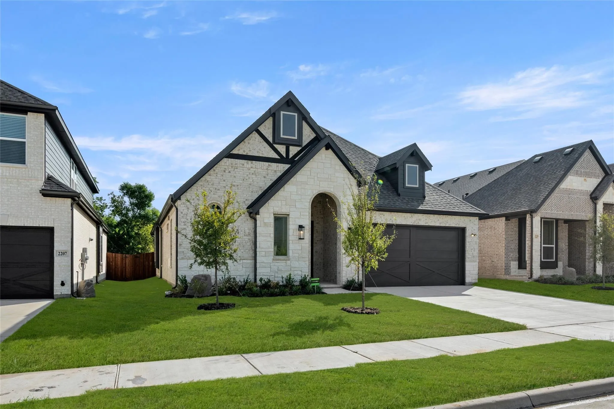 View of front of property featuring roof with shingles, driveway, stone siding, brick siding, and a garage