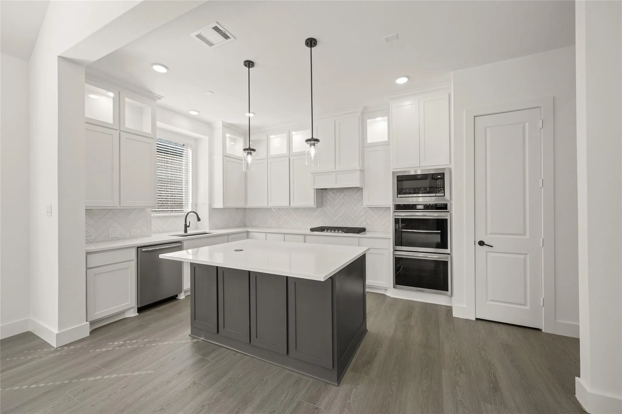 Two tone kitchen with stainless steel appliances, glass insert cabinets, two tone cabinetry, tasteful backsplash, and hanging light fixtures