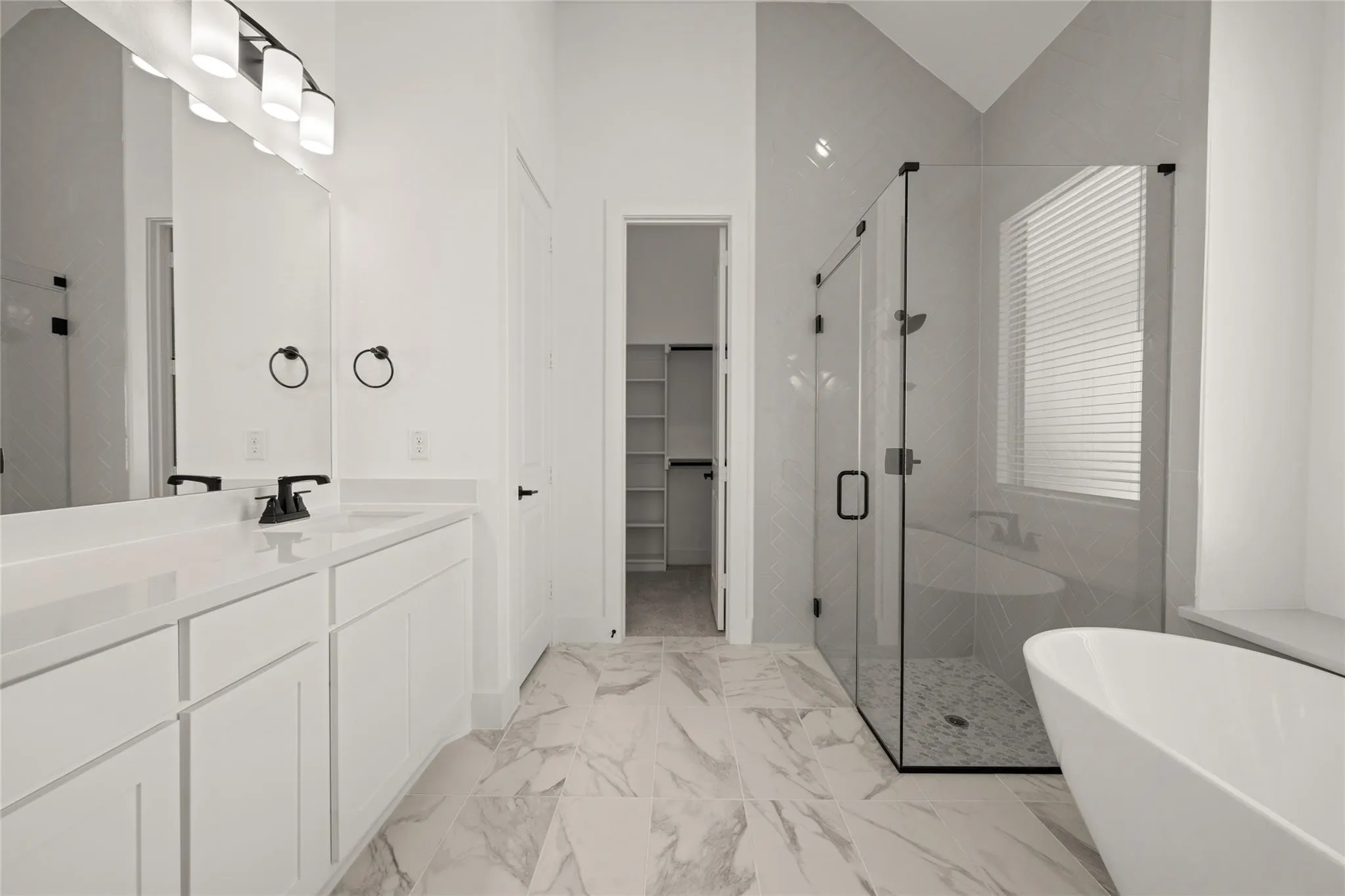Bathroom with a stall shower, a freestanding tub, vanity, a walk in closet, and light marble finish floors