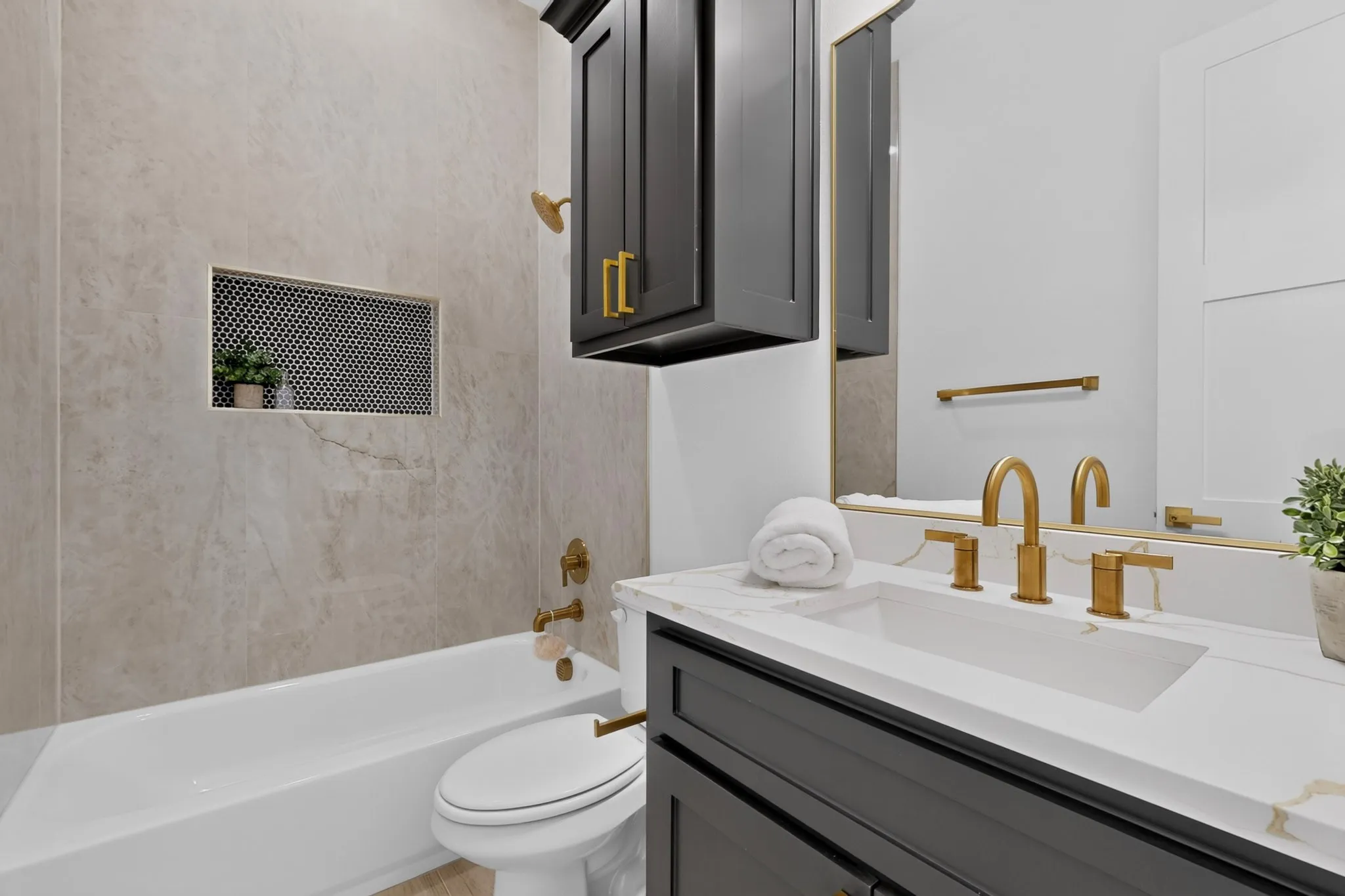 Contemporary bathroom featuring a white porcelain tub, a tiled shower niche with mosaic accent, a vanity with dark cabinetry, a white countertop with integrated sink, and brass fixtures