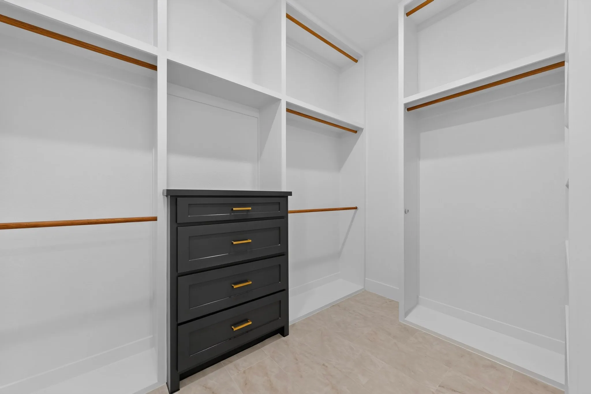 Custom closet organization system featuring white shelving, multiple hanging rods, and a built-in four-drawer dresser with gold-tone hardware