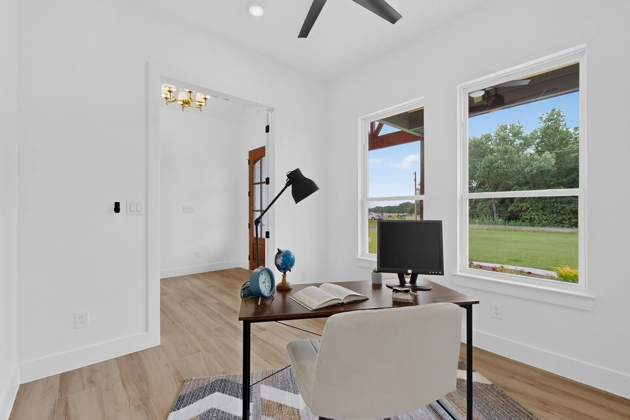 Dedicated office space featuring bright white walls, wood-finish flooring, two large windows, a ceiling fan, and a recessed light