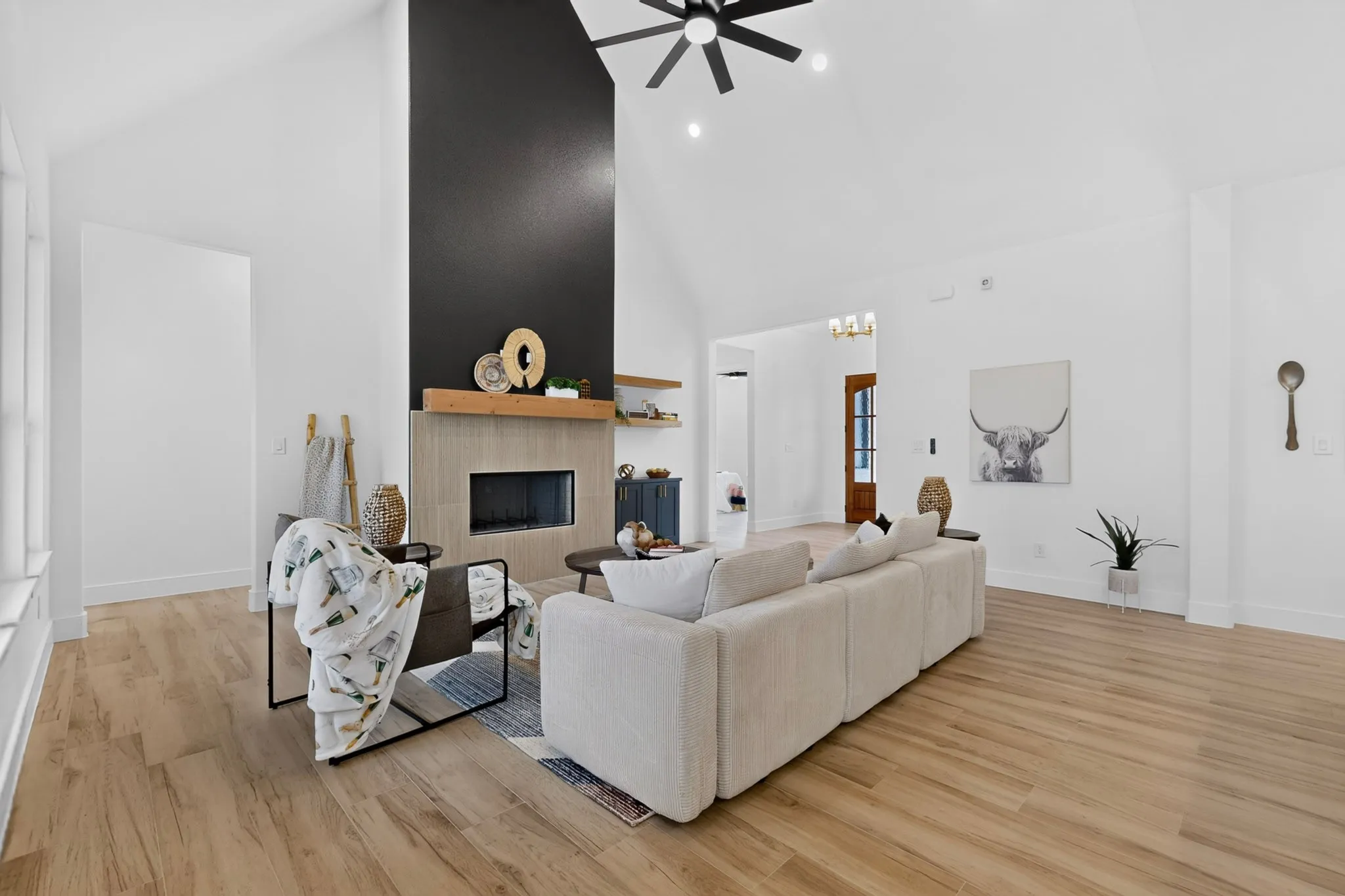 Spacious living area featuring vaulted ceilings, wood-finish flooring, a contemporary fireplace with a stone surround, an integrated wood mantel, and a ceiling fan