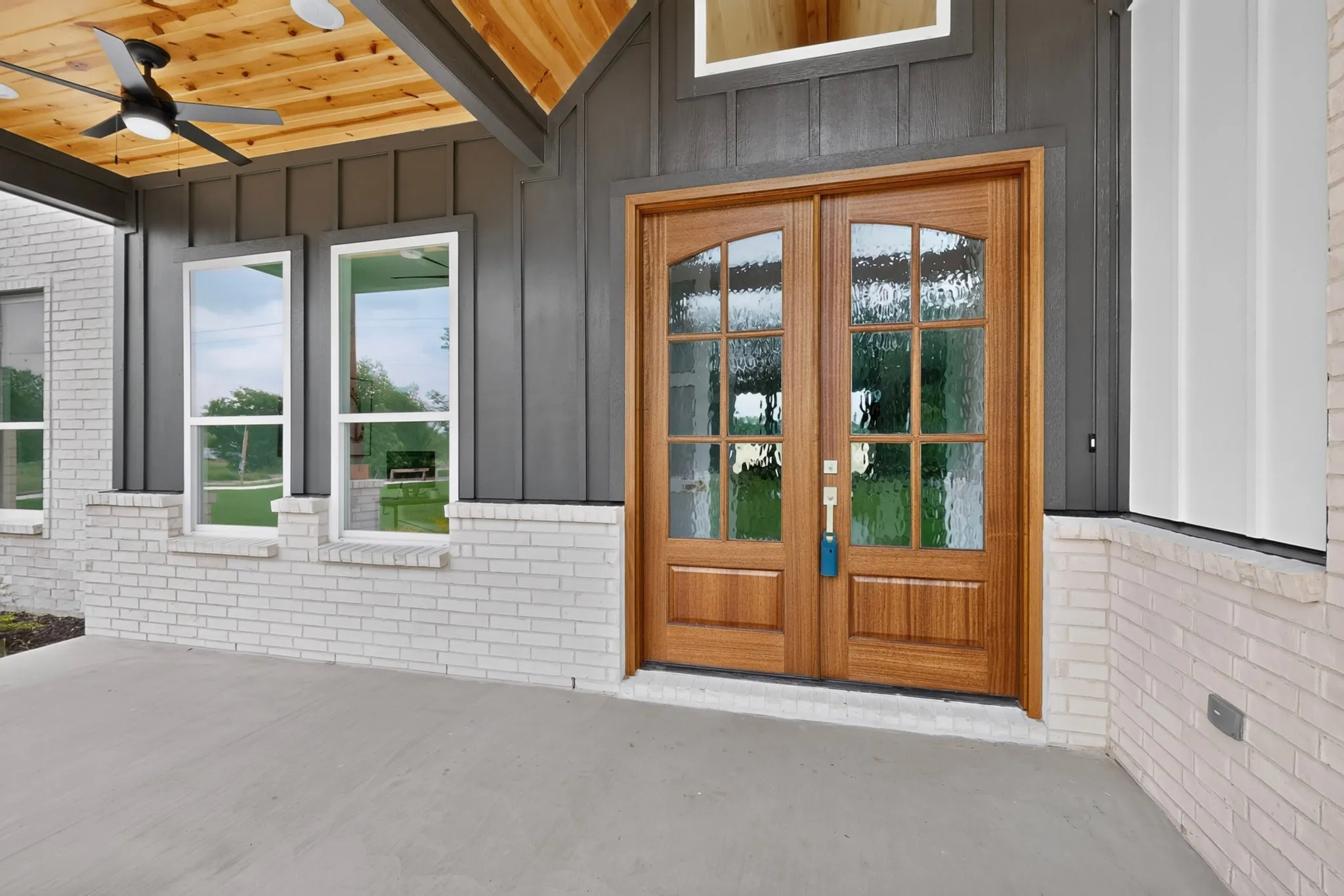 Entryway featuring double wood-finish doors with decorative glass inserts, gray vertical siding, and a white brick facade