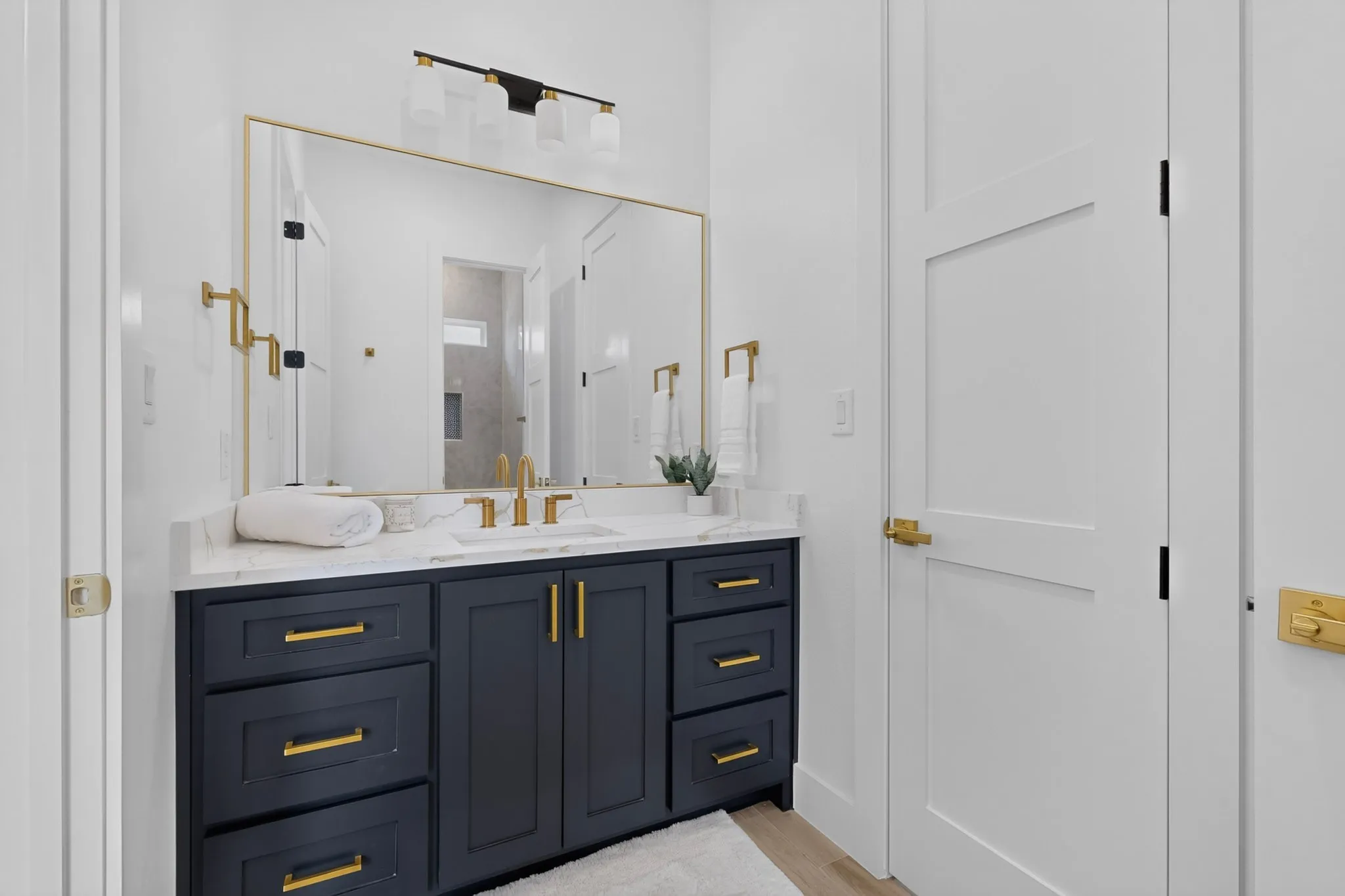 Modern bathroom featuring a dark blue vanity with gold hardware, a white countertop, and a rectangular gold-framed mirror
