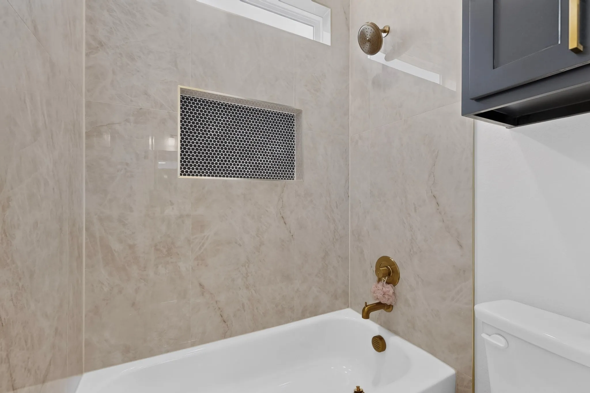 Bathtub with brass fixtures, light-toned tile surround, and an integrated shower niche featuring mosaic tile