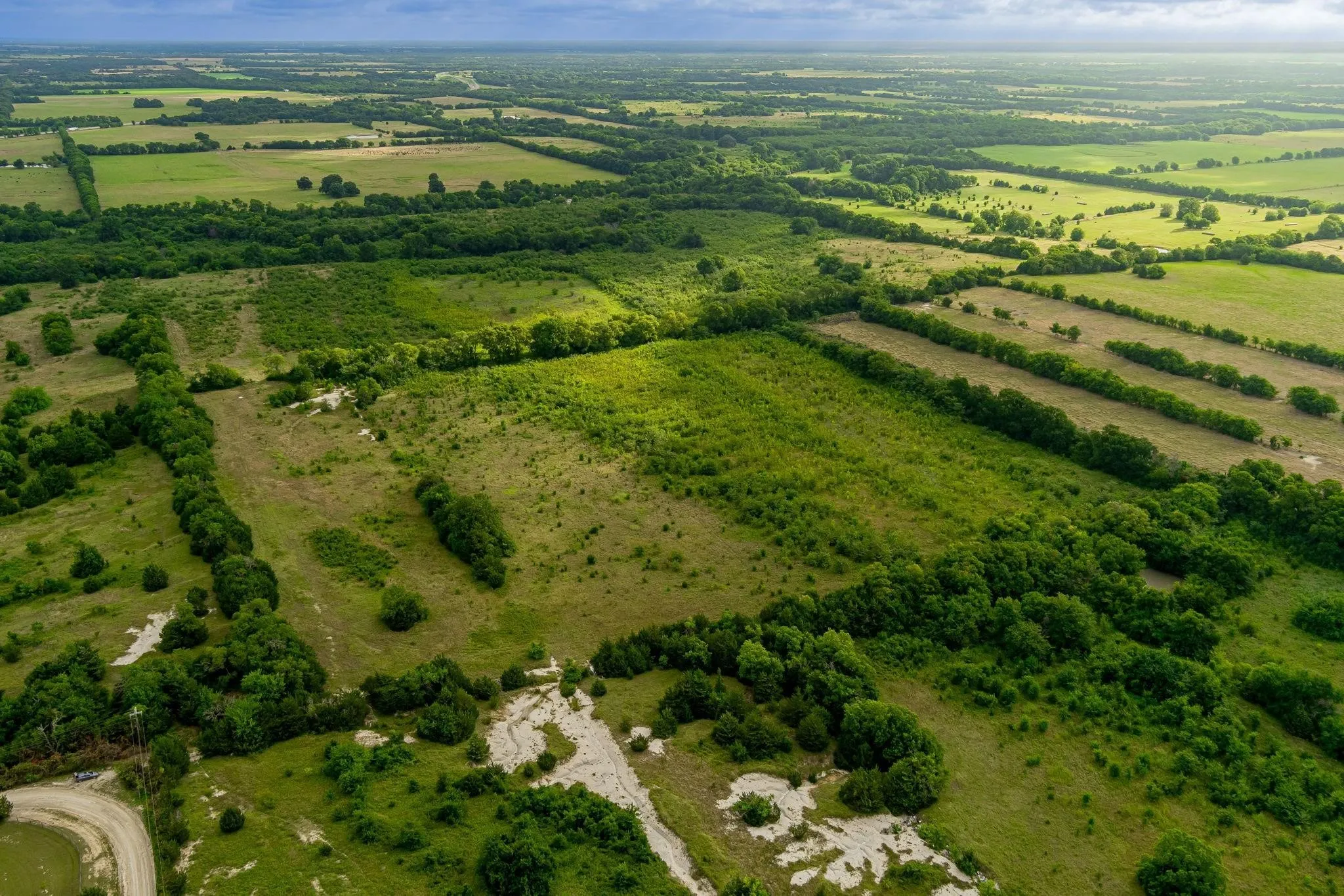 Expansive rural landscape featuring extensive green fields and varied tree lines
