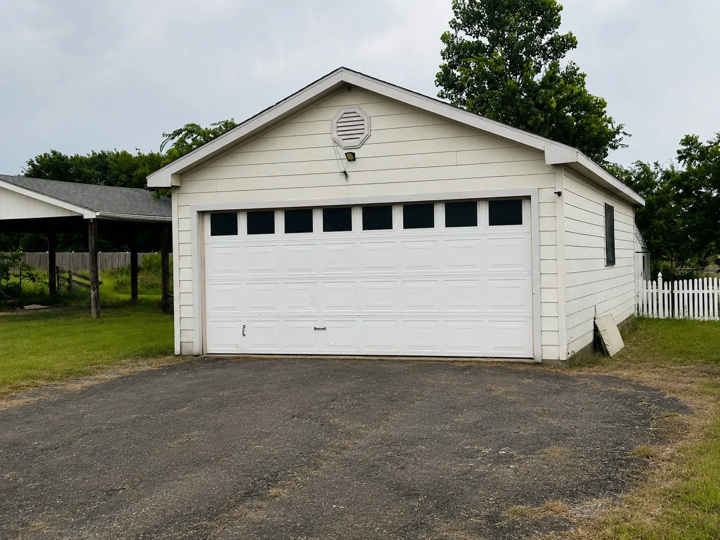 Detached garage with horizontal siding, a paneled garage door, and a gable roof with an octagonal vent