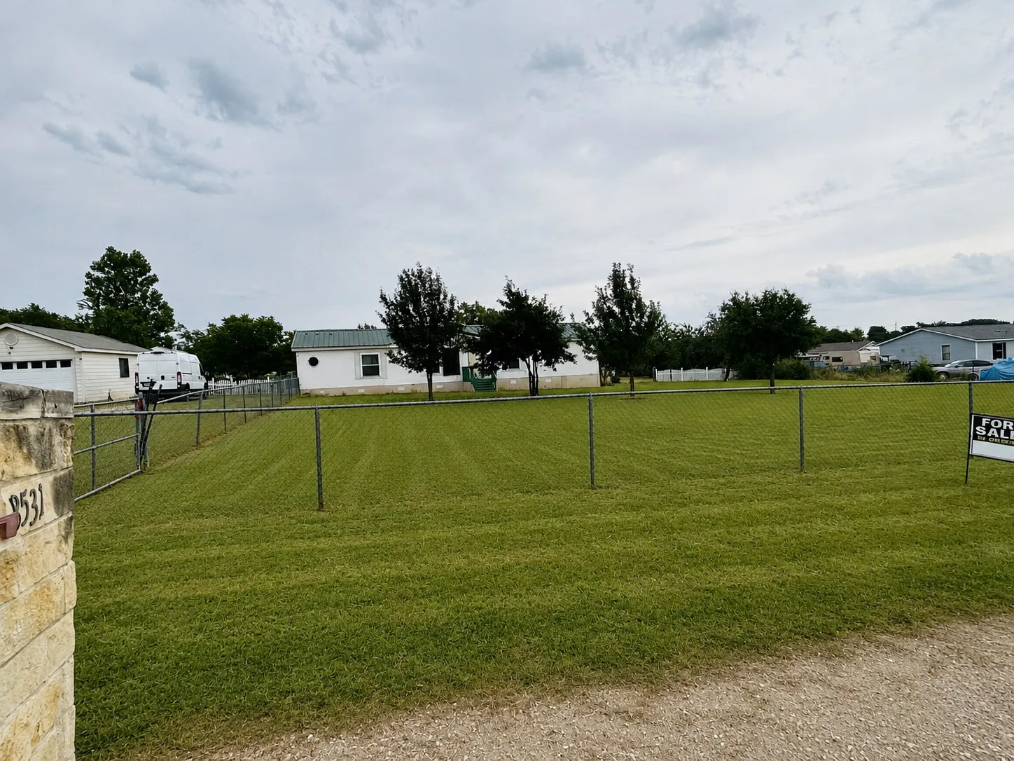 Expansive grassy lot featuring mature trees and chain-link fencing