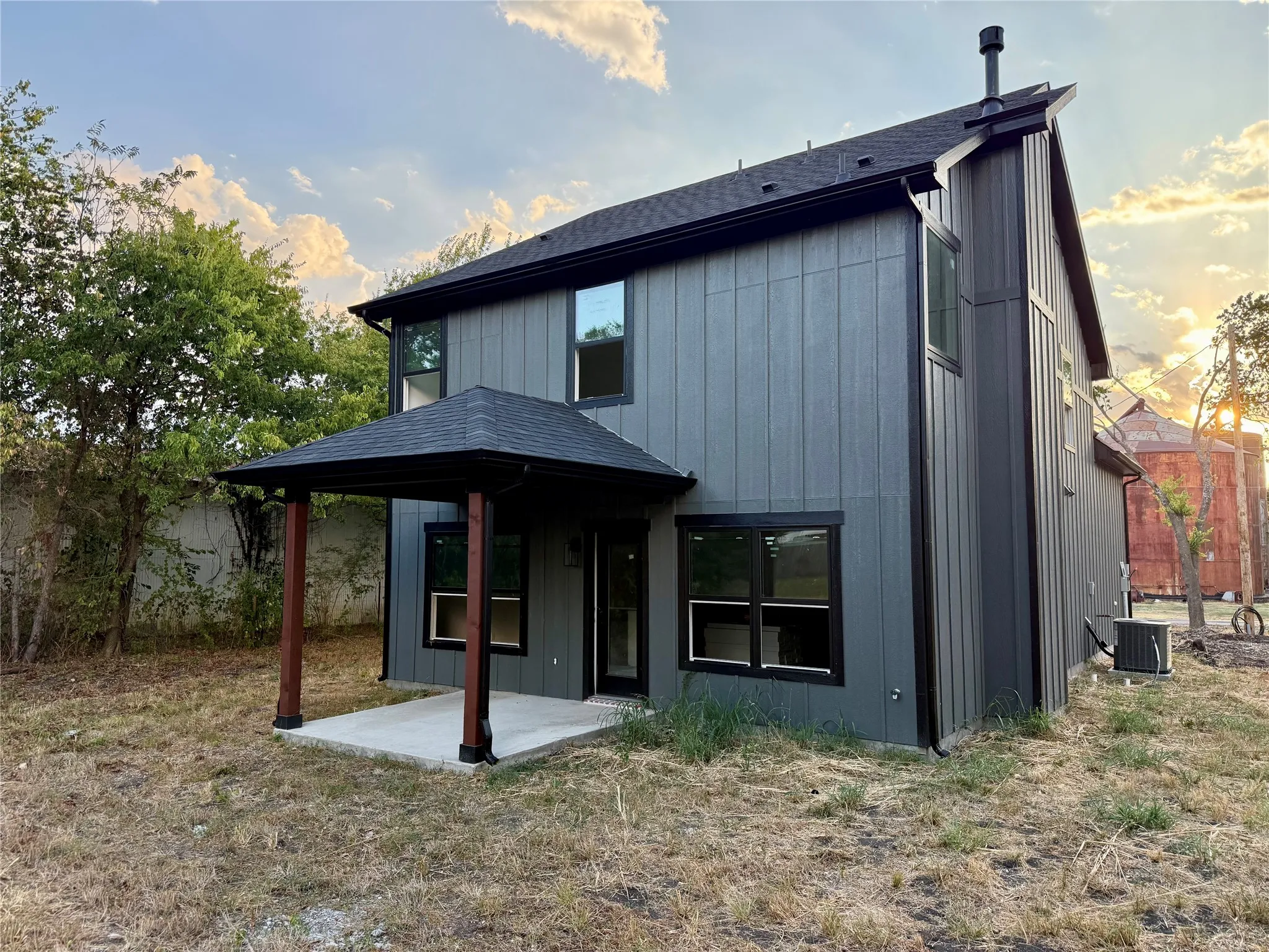 Board and batten exterior with black trim windows, covered concrete patio with wood posts, and a dark shingle roof
