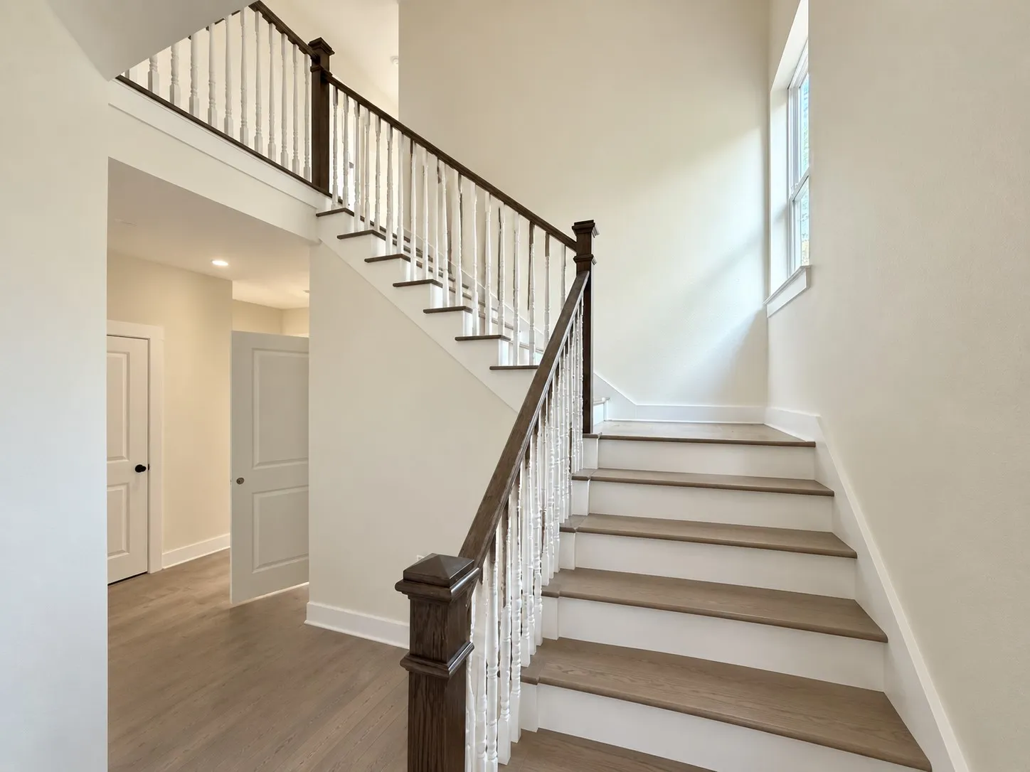 Two-story staircase with wood-finish treads, white risers, and dark wood handrails