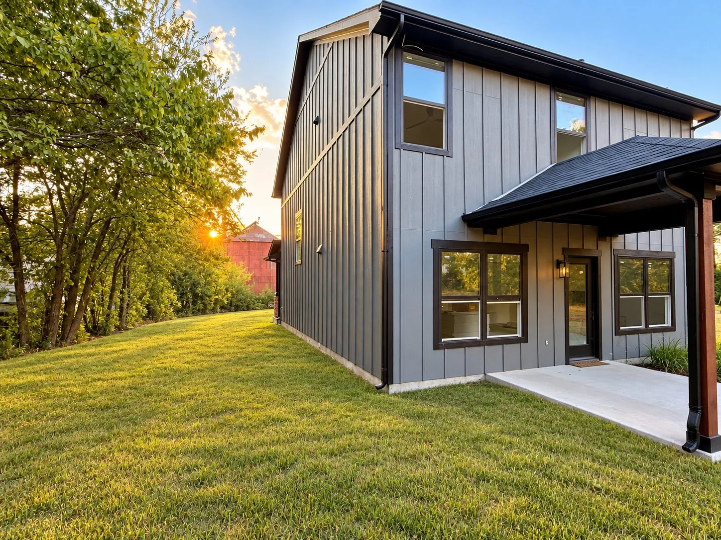 Board and batten exterior with dark trim windows, covered concrete patio, and a spacious grassy yard