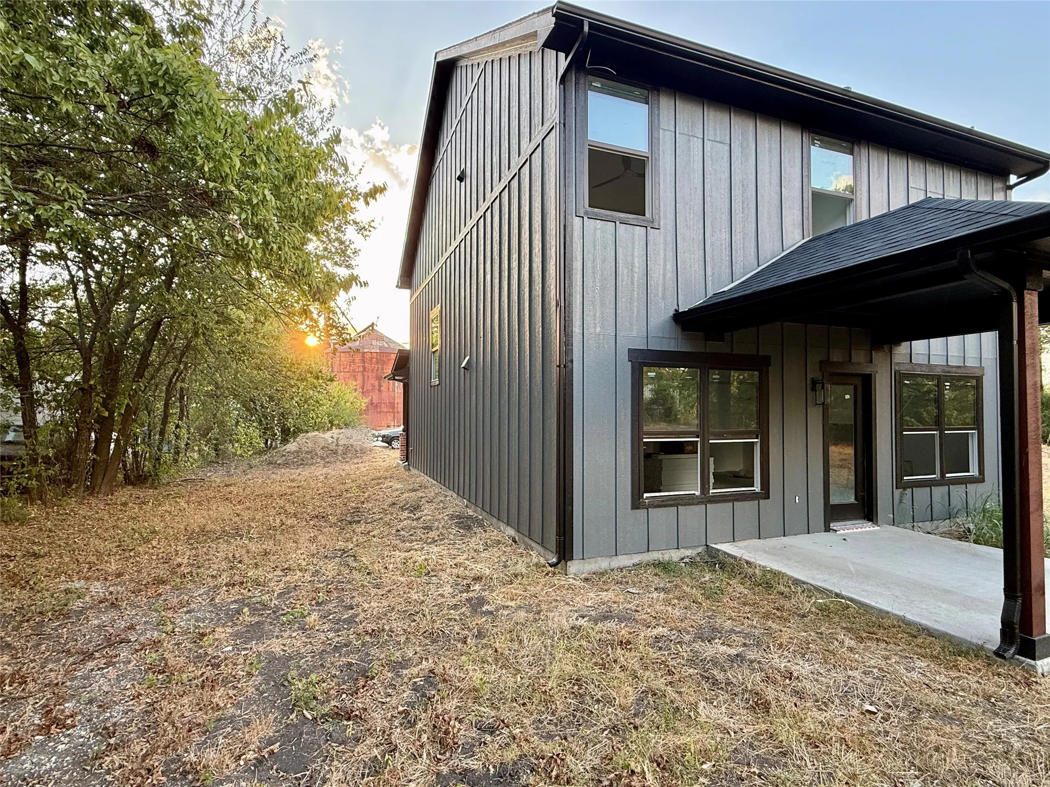 Vertical board siding with dark trim, covered patio, and concrete slab