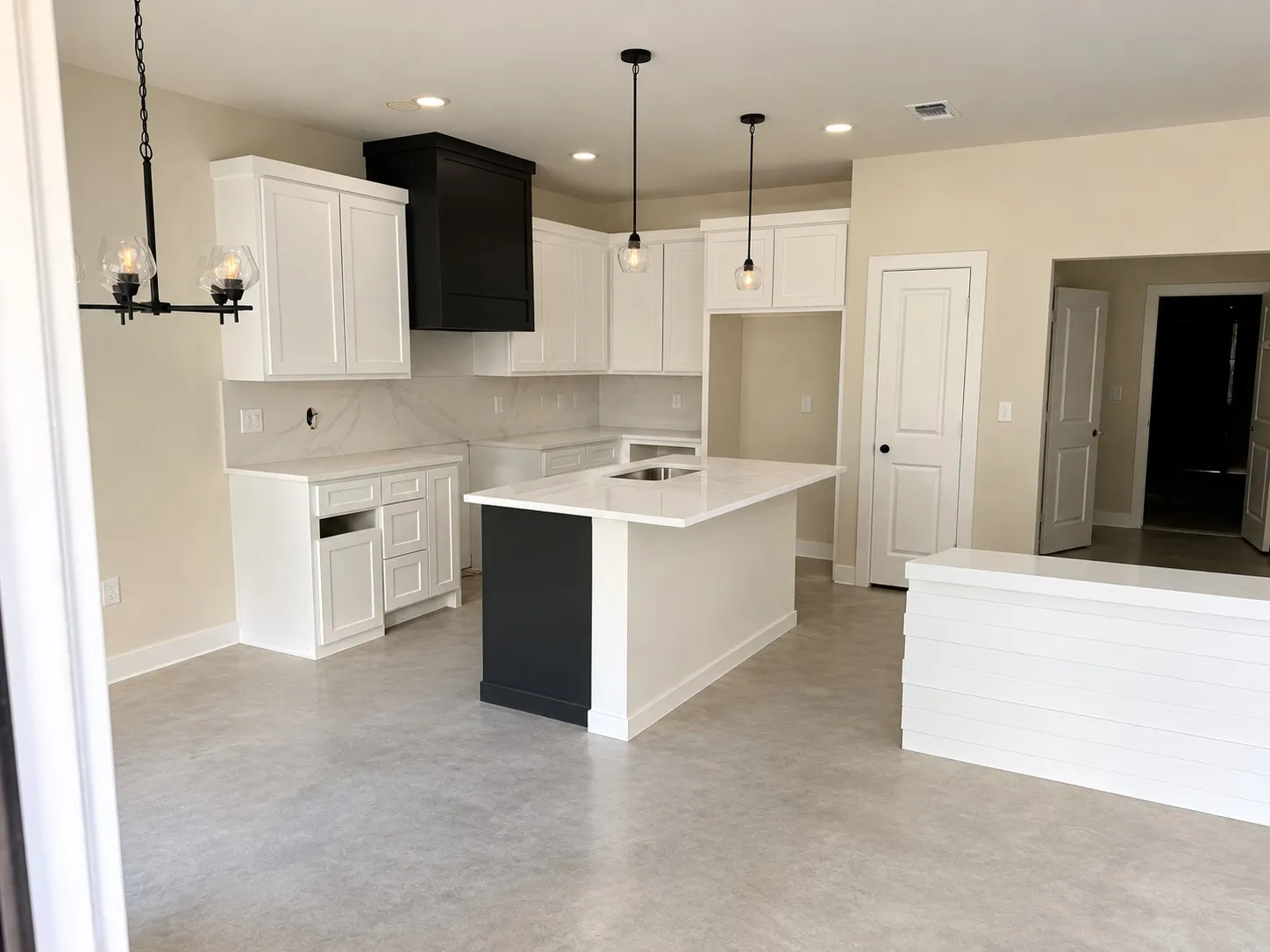 Modern kitchen featuring white cabinetry, a black range hood, a kitchen island with integrated sink, pendant lighting, and light-toned flooring