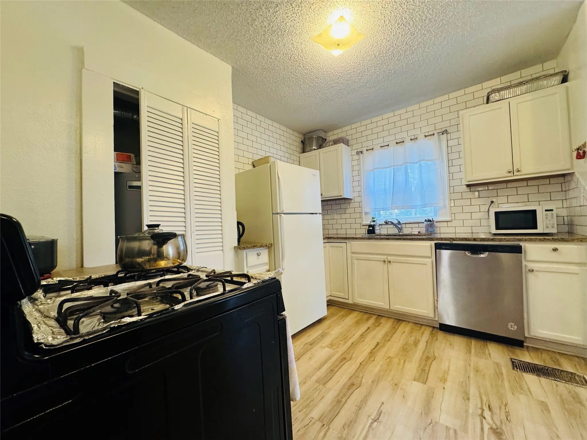 Kitchen featuring wood-finish flooring, white cabinetry, speckled countertops, subway tile backsplash, and a stainless steel dishwasher