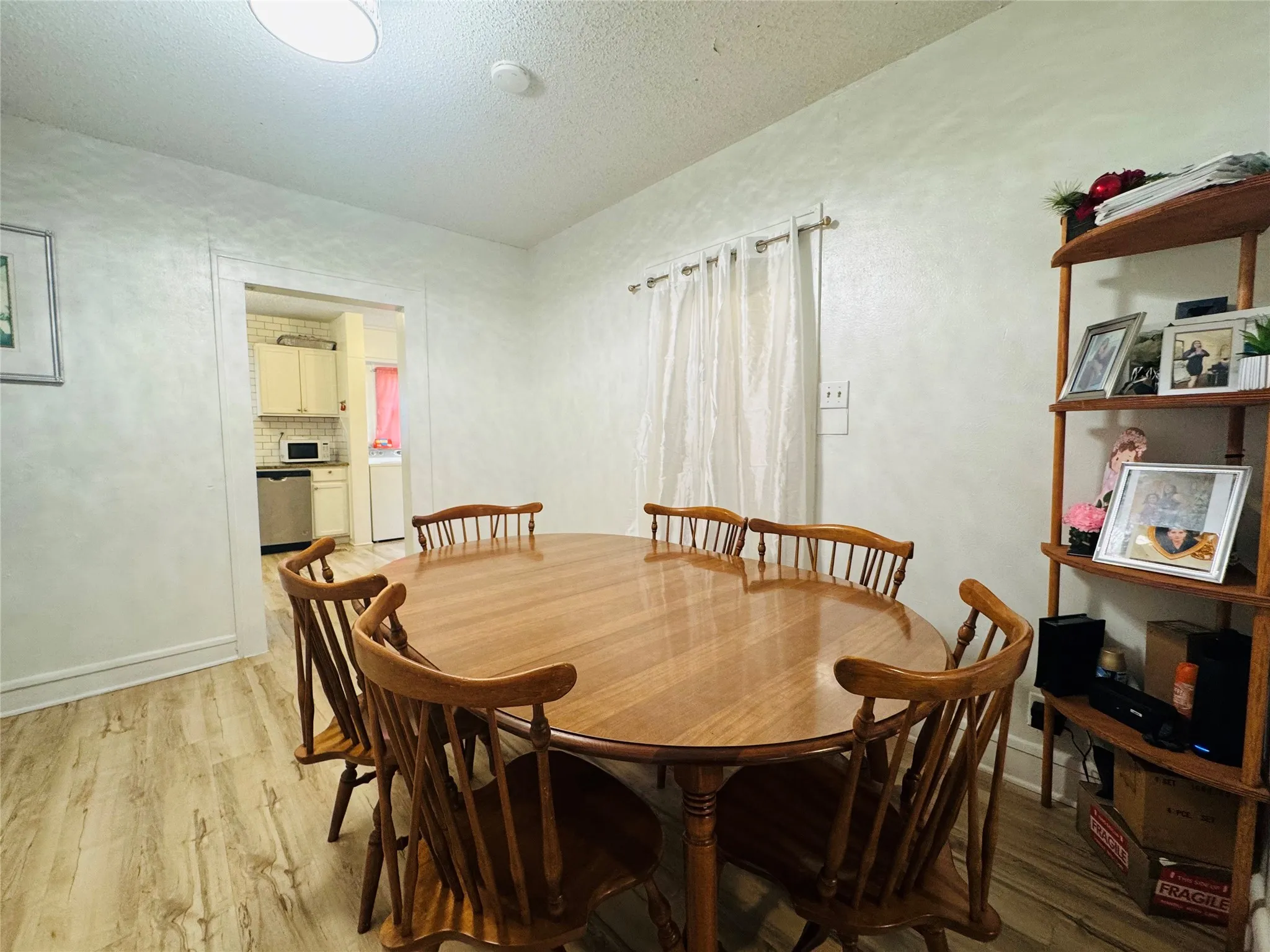 Dining area featuring wood-finish flooring, light-toned walls, and a window with sheer curtains