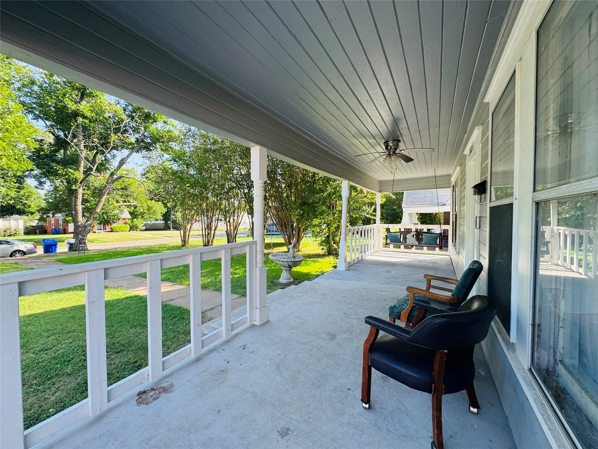 Expansive covered porch featuring a concrete surface, white railing, and a ceiling fan