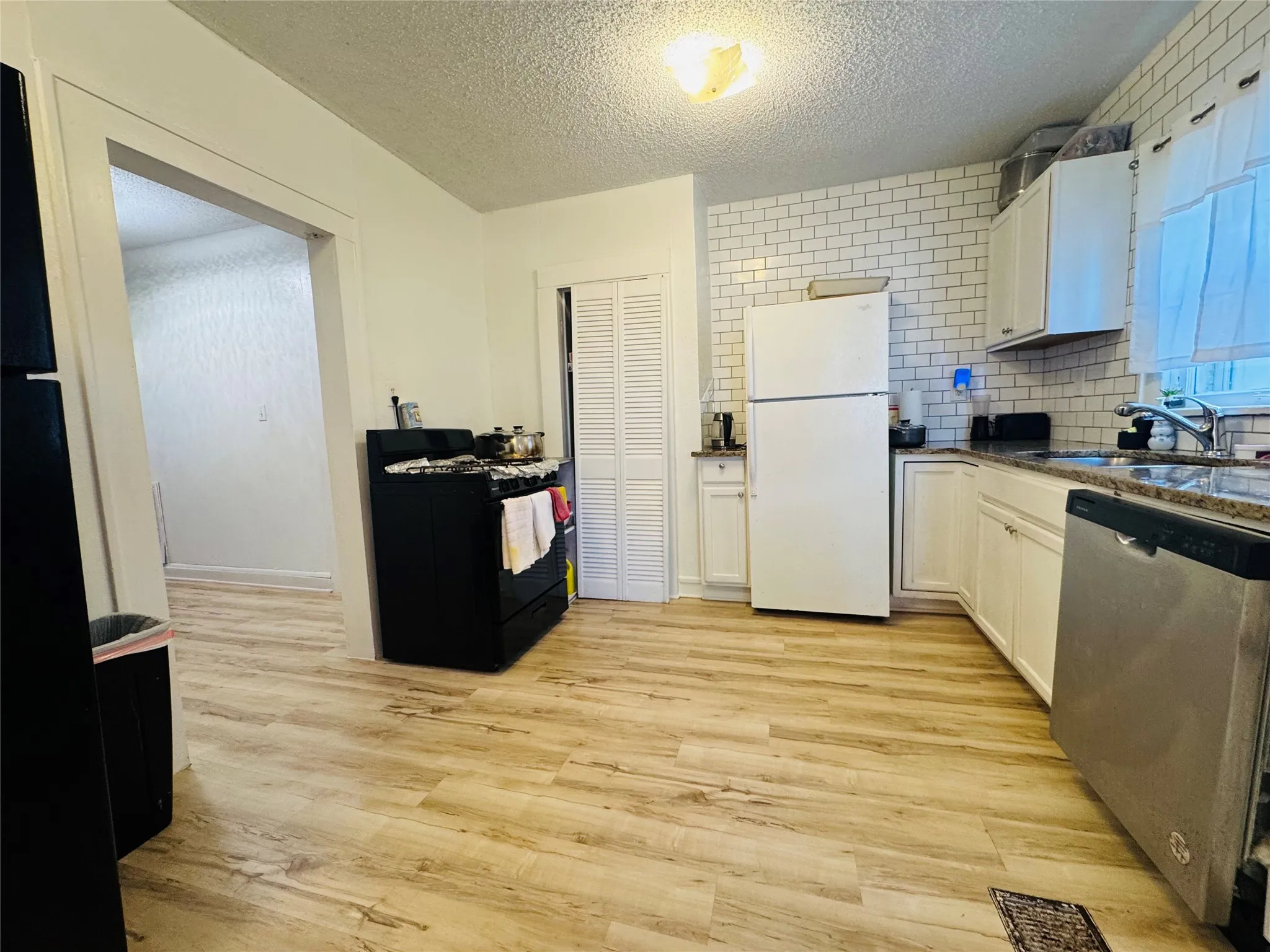 Kitchen featuring wood-finish flooring, white cabinetry, subway tile backsplash, and stone-finish countertops