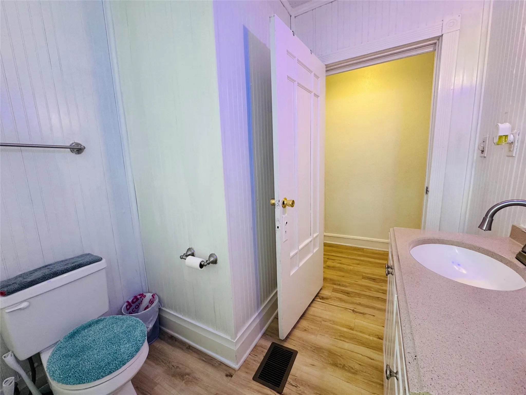 Powder room featuring wood-finish flooring, white beadboard paneling, and an integrated sink vanity with a light-colored countertop