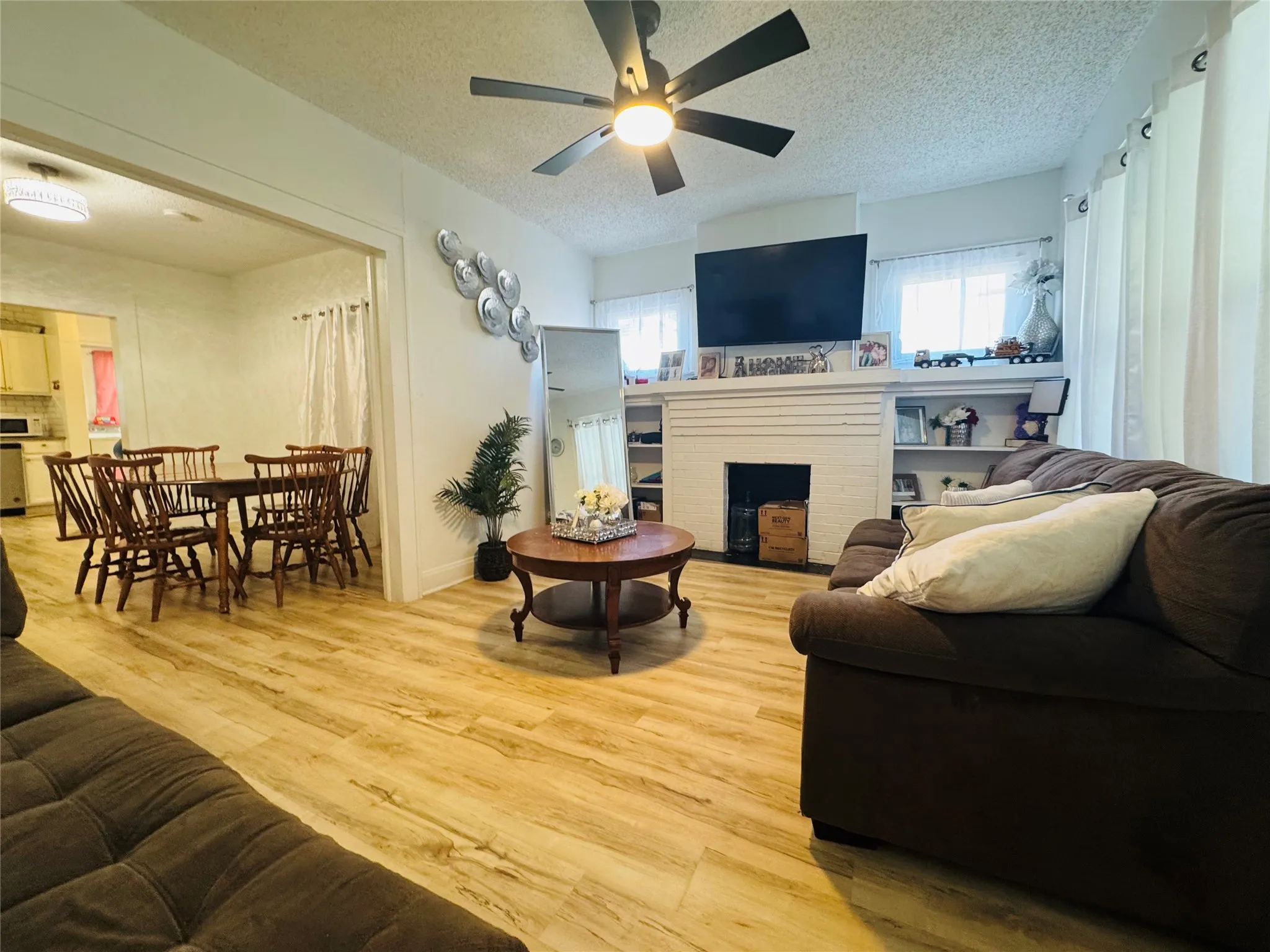 Open concept living area featuring wood-finish flooring, a ceiling fan with integrated lighting, and a decorative fireplace with built-in shelving