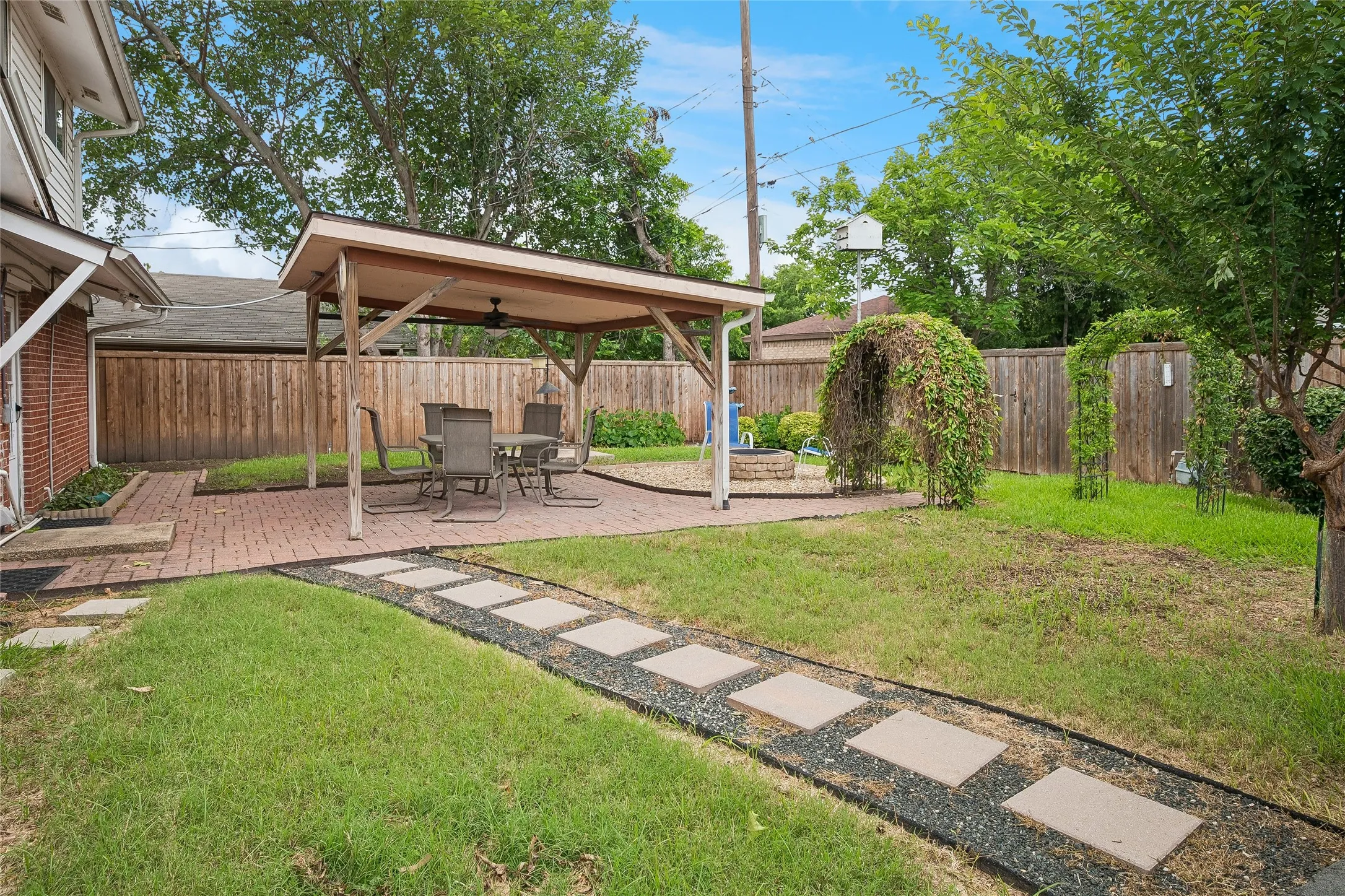 Backyard oasis with covered paver stone patio, gravel surround stepping stone path and vine-draped arbors.