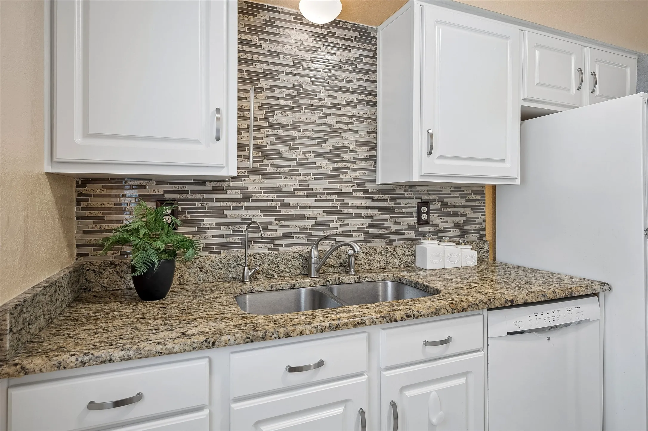 Beautiful counter to ceiling mosaic tile backsplash and Bosch dishwasher.