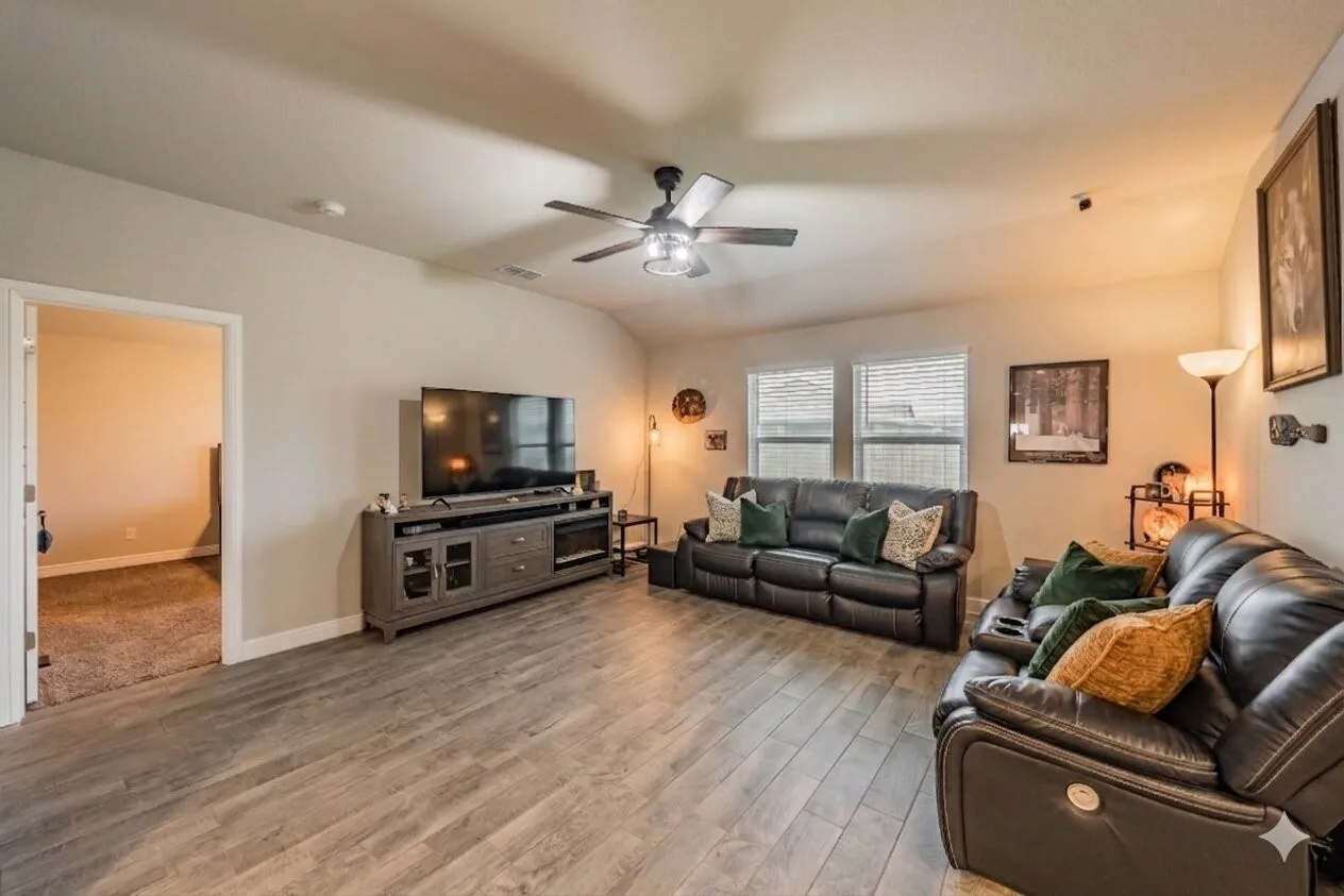 Spacious living area featuring ceramic plank tile, vaulted ceilings, a ceiling fan, and abundant natural lighting