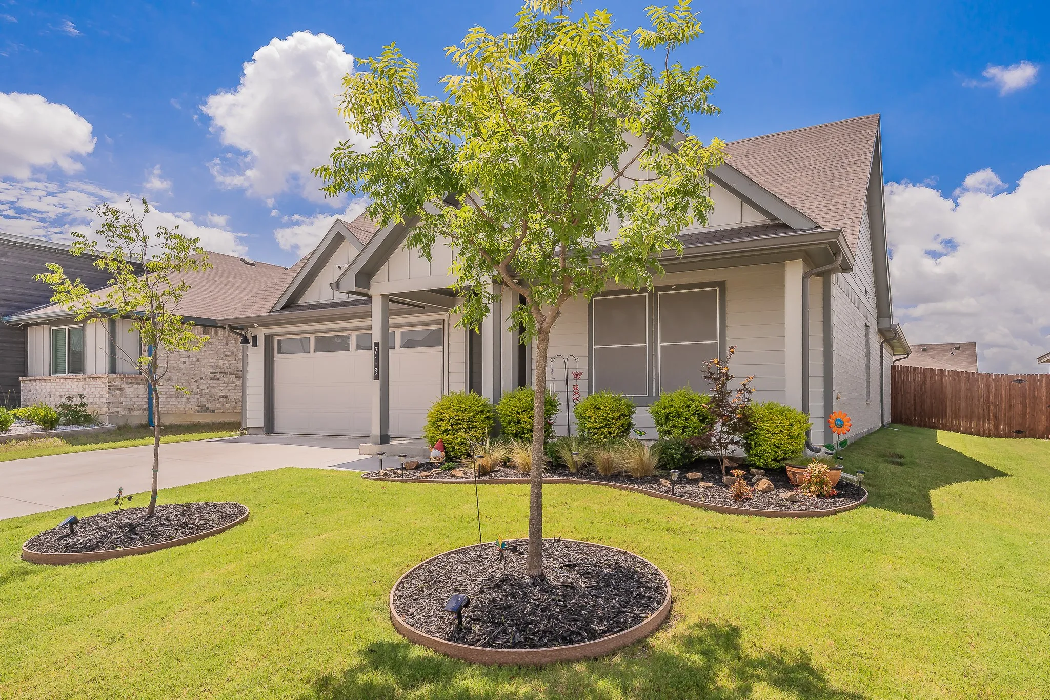 Single-family residence featuring a two-car garage, manicured lawn, and mature trees