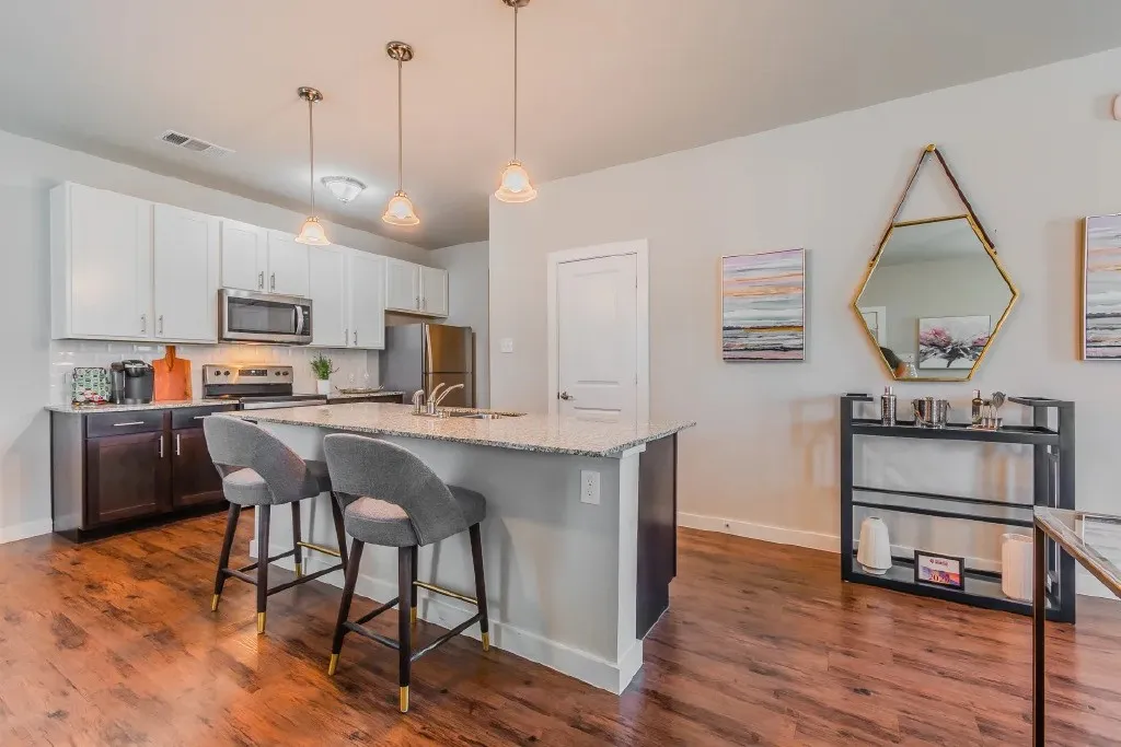 Kitchen featuring an island with stone countertops, stainless steel appliances, white upper cabinetry, dark lower cabinetry, and wood-finish flooring