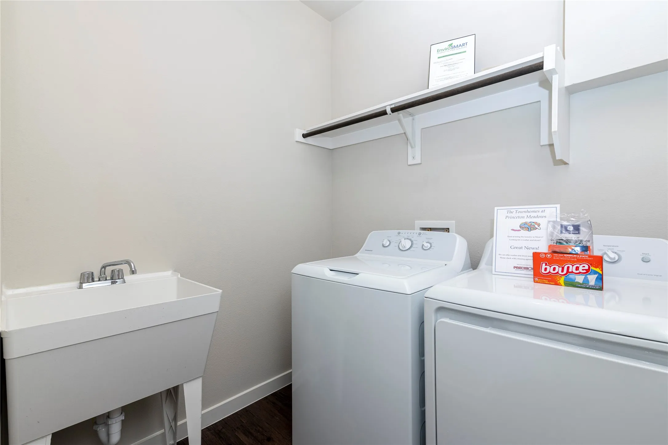 Dedicated laundry area featuring a utility sink with chrome faucet, overhead shelving, and dark wood-finish flooring