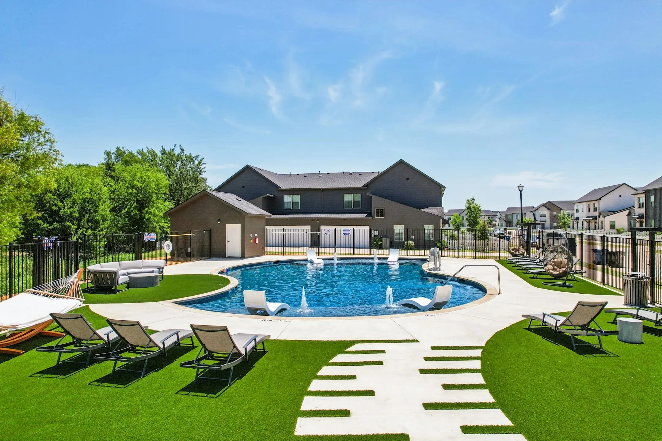 Resort-style pool area featuring a freeform swimming pool with in-pool lounge seating, surrounding concrete decking, and artificial turf landscaping with decorative stepping stones