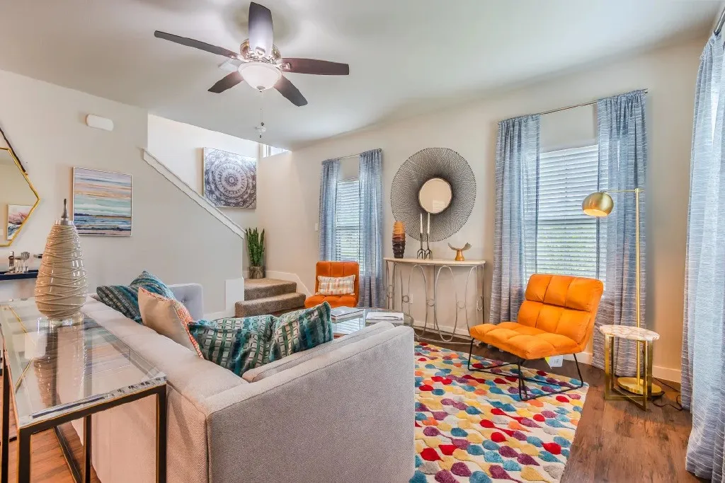 Living area featuring wood-finish flooring, a ceiling fan, and multiple windows with blinds