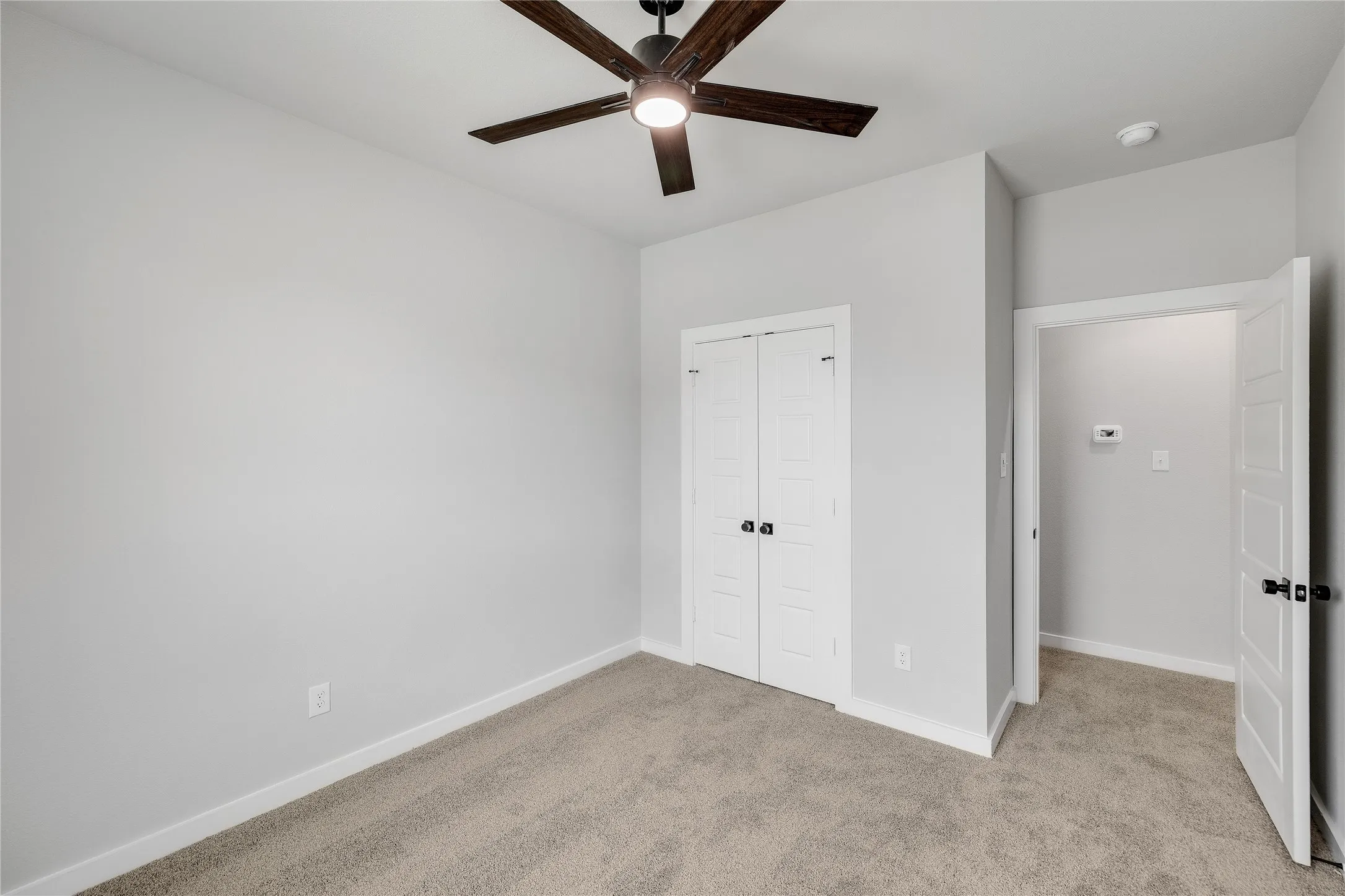 Neutral-toned room featuring a ceiling fan with light, light gray carpeting, and white trim