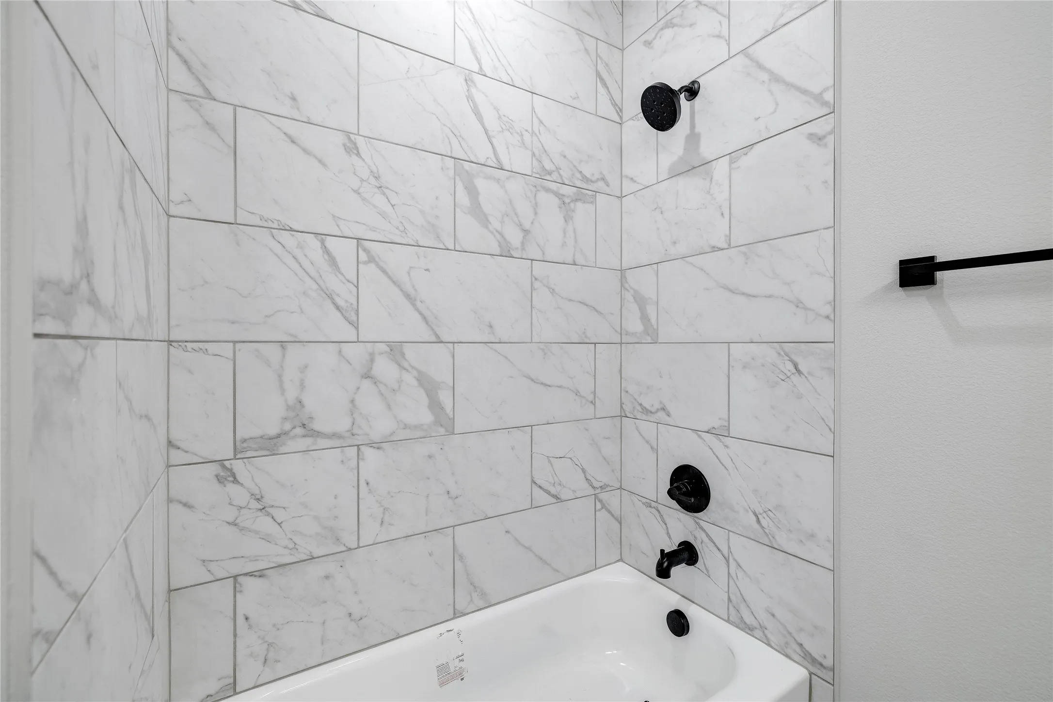 White subway tile with gray veining surrounds a built-in bathtub with matte black fixtures, including a showerhead, faucet, and drain