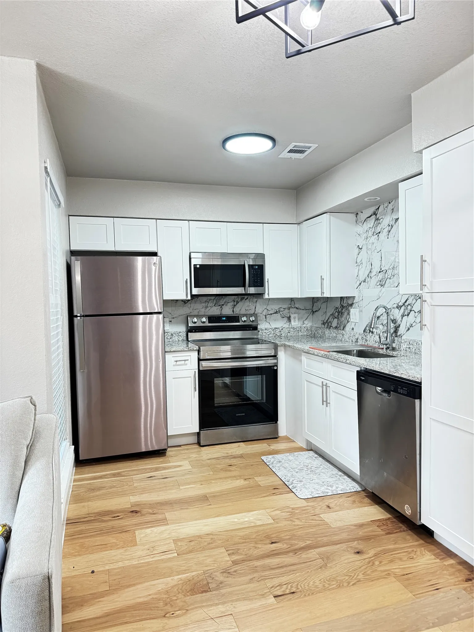 Kitchen featuring white cabinetry, granite-style countertops, stainless steel appliances, and a marble-patterned backsplash